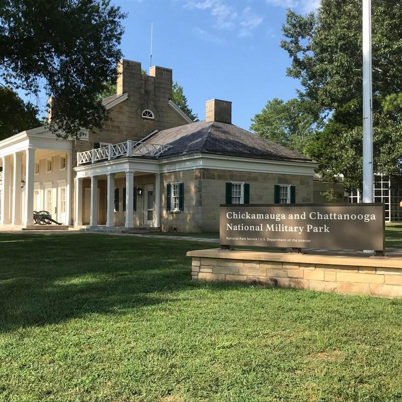 Large stone building with columns, green lawn, and trees under bright sunlight.