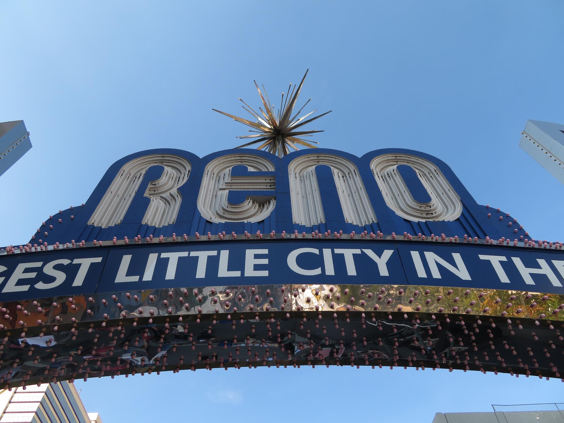 Large blue sign with 'RENO' and starburst, 'EST LITTLE CITY' text, under clear sky.