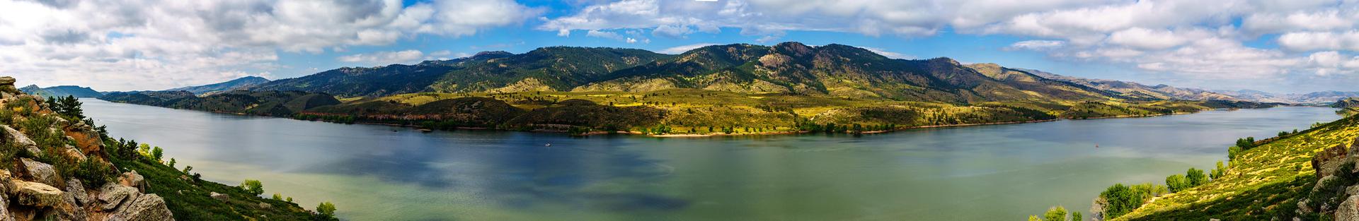 Panoramic view of a wide lake surrounded by green and brown mountains.