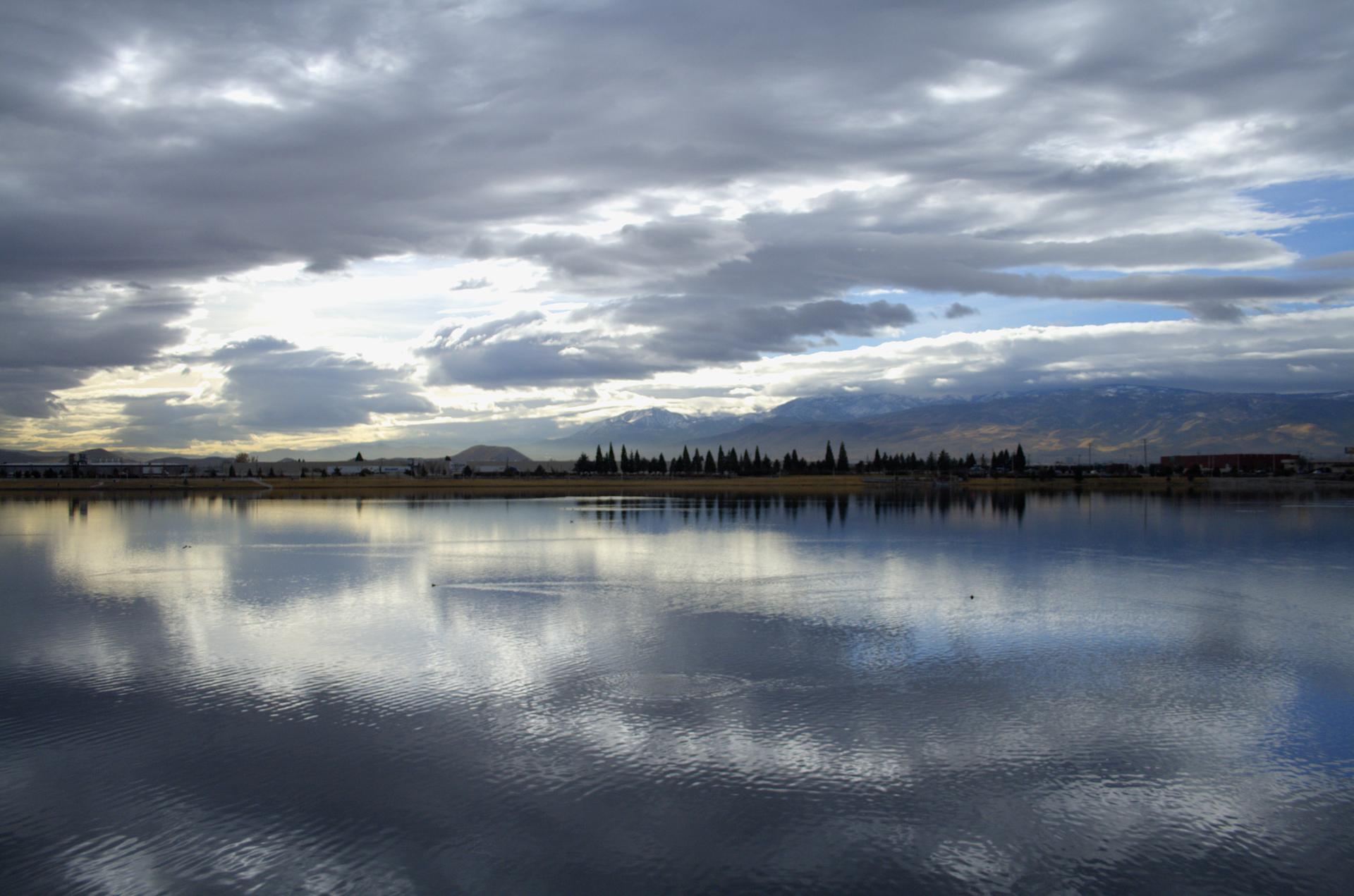 Wide lake reflecting a cloudy sky and distant mountains.