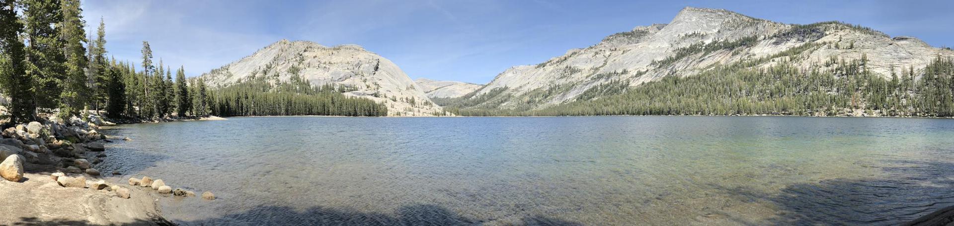 Panoramic view of a clear lake bordered by pine trees and granite mountains.