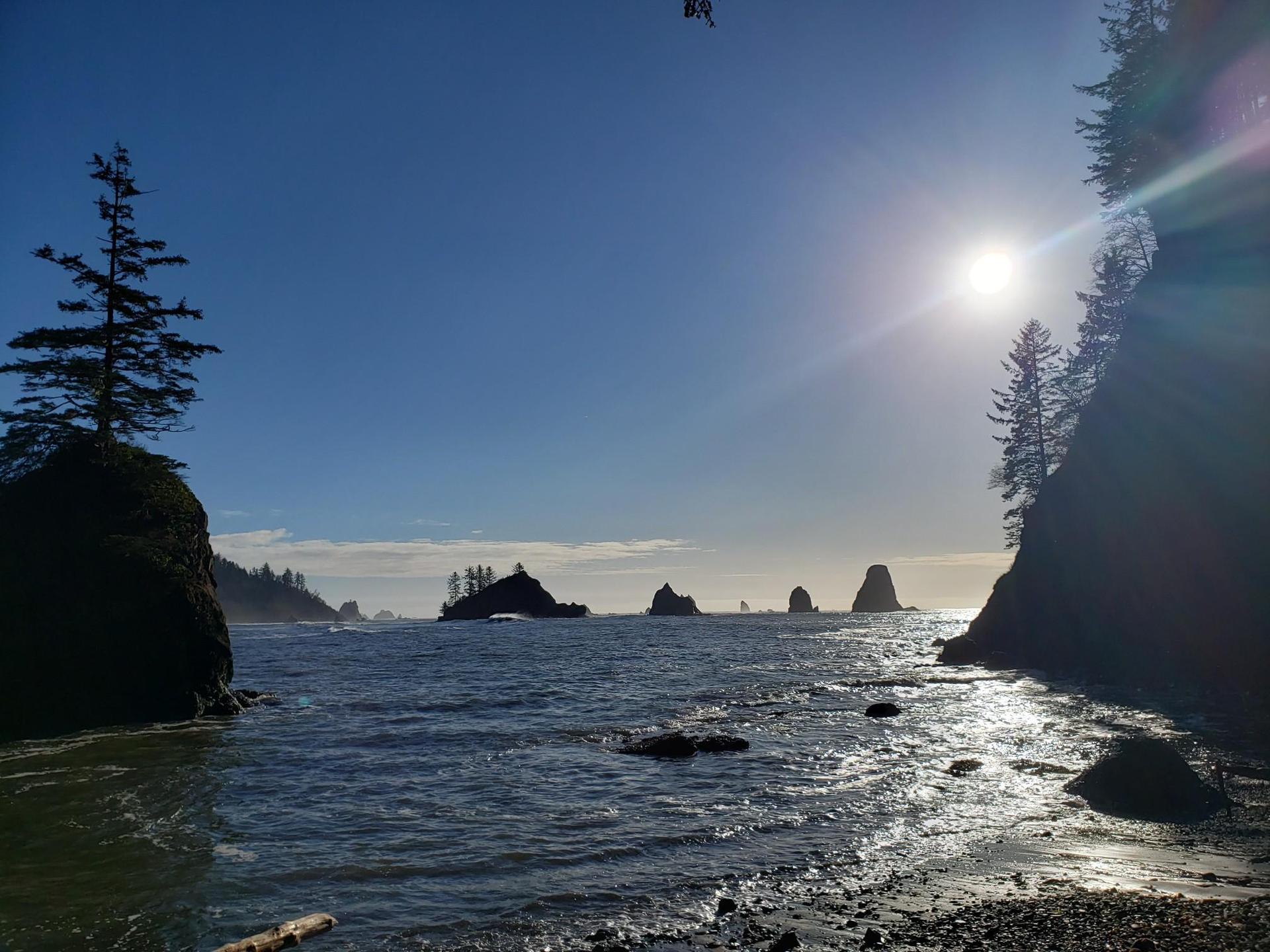 Bright sun over ocean bay with sea stacks and rocky shore.