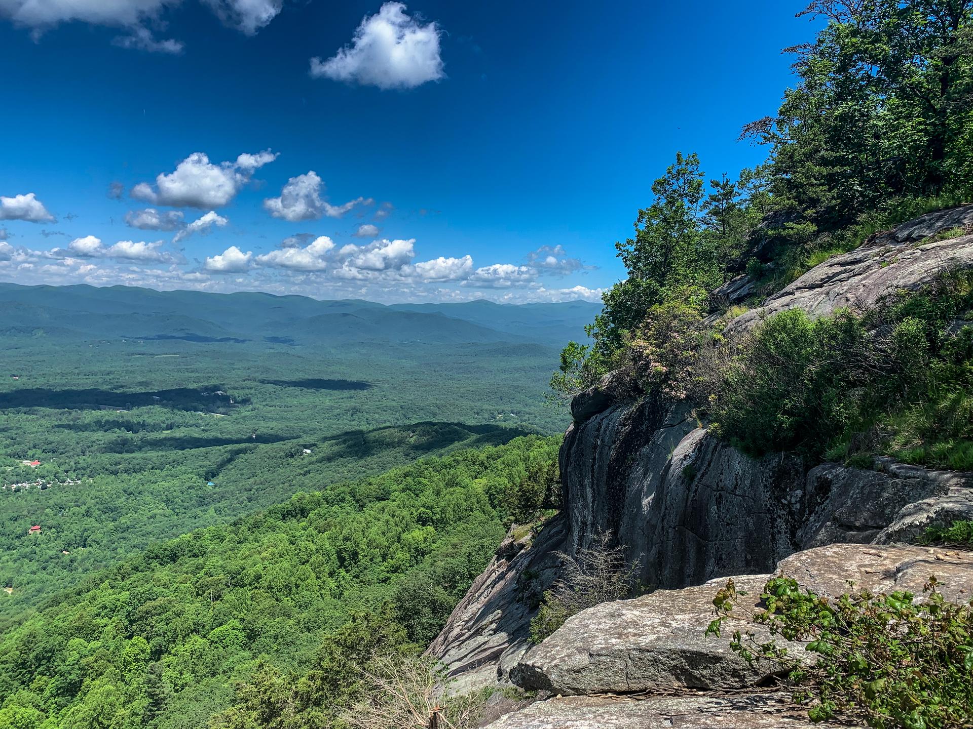 Expansive mountain vista from a rocky cliff on a bright, sunny day.
