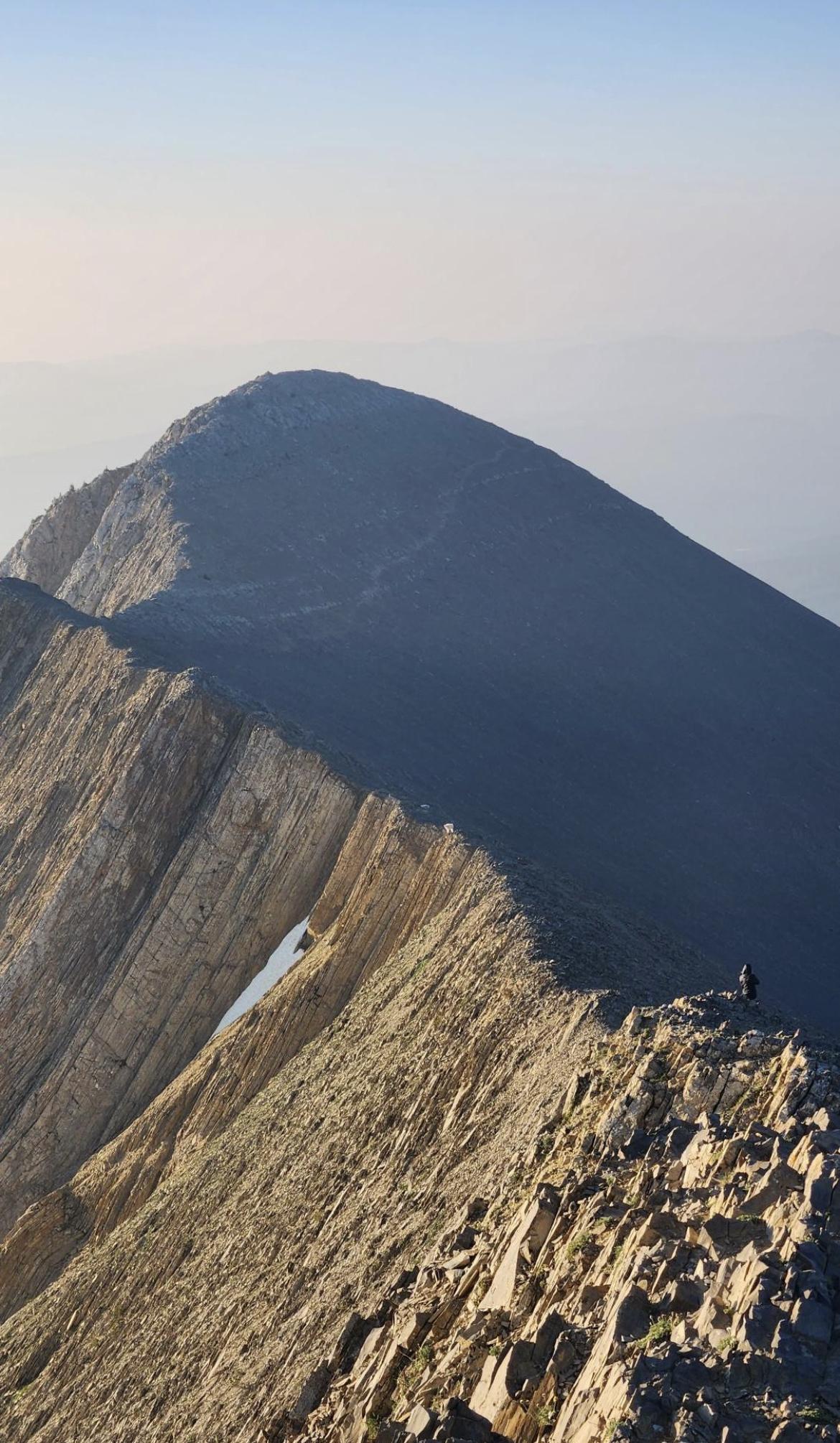 A hiker on a sunlit, rocky mountain ridge under a clear sky.