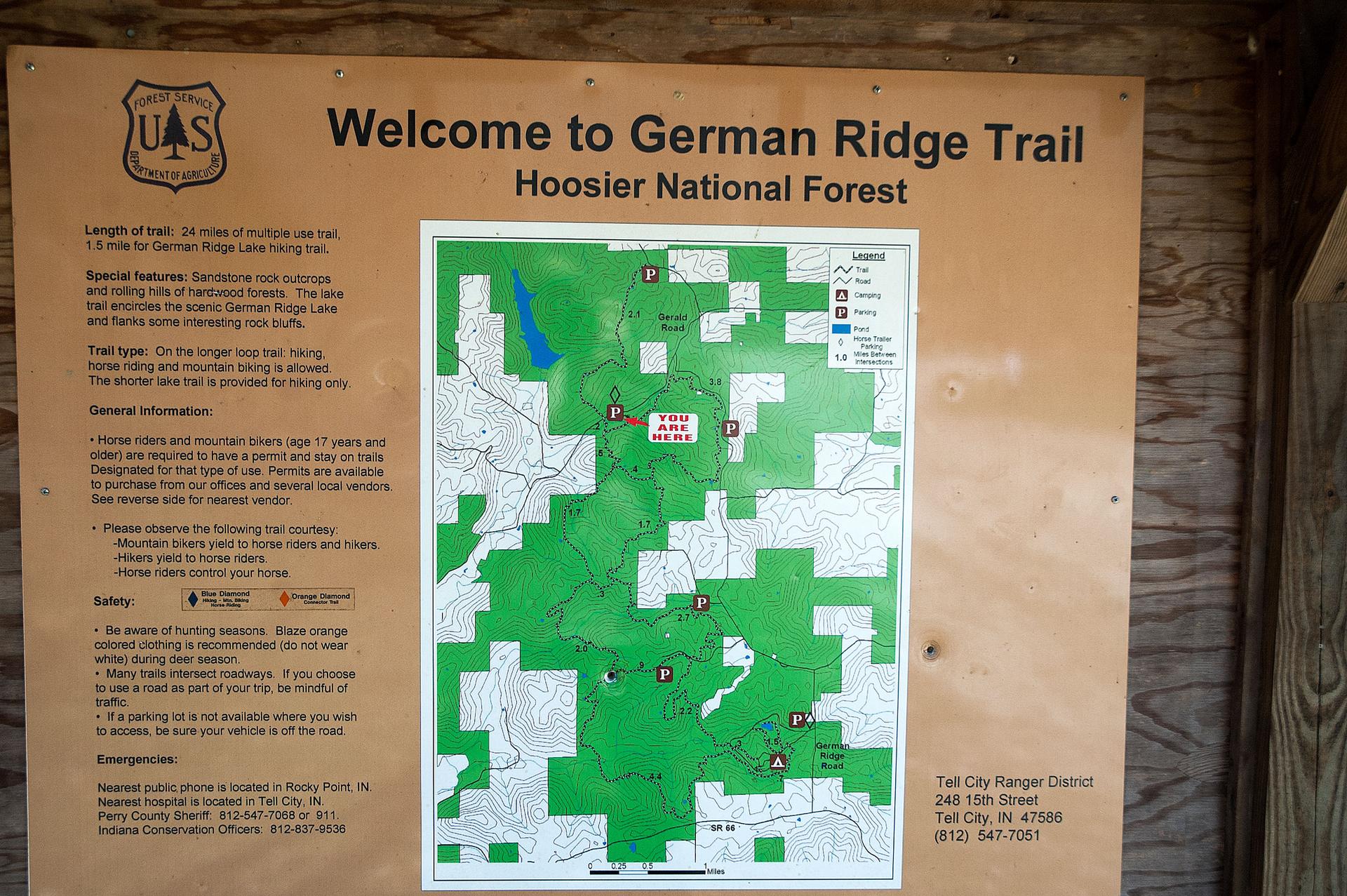 A large wooden information sign displays a trail map and text outdoors.