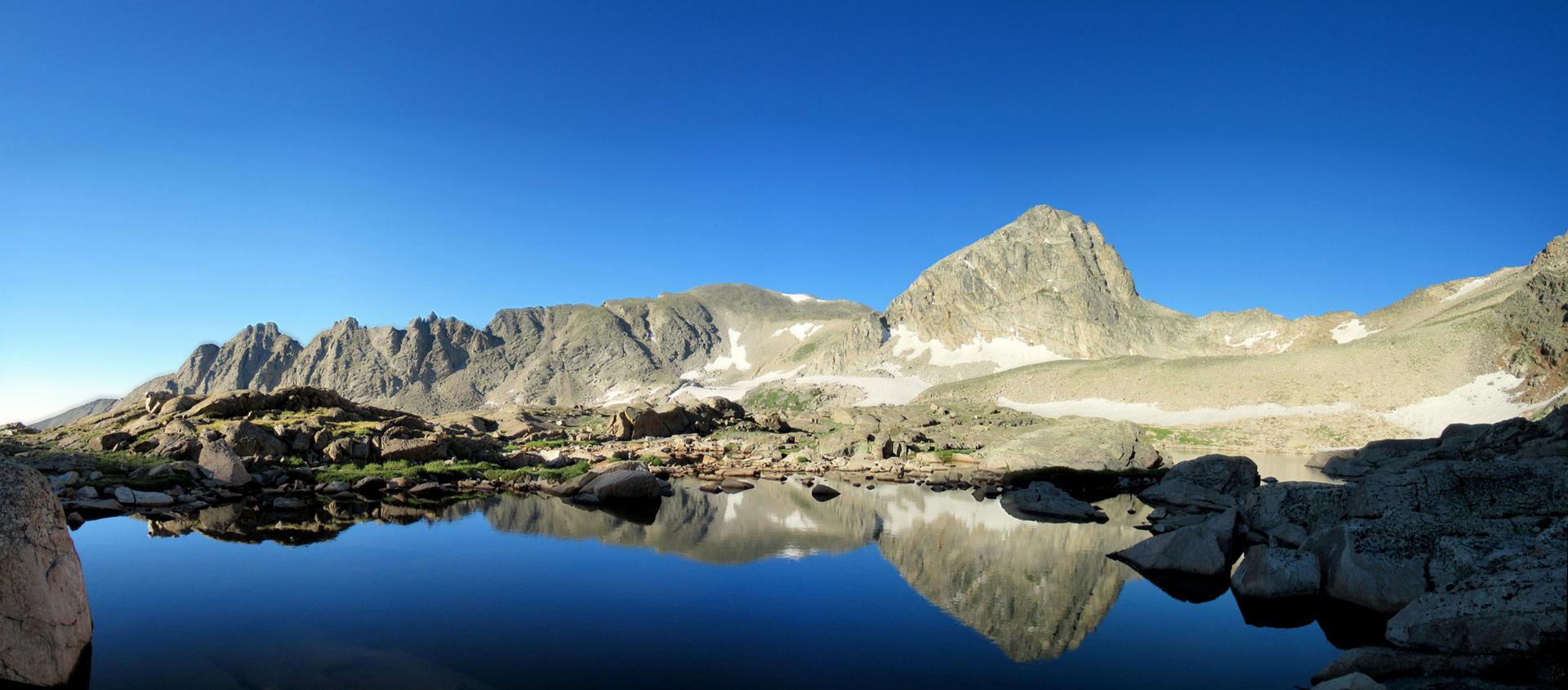 Panoramic view of rugged mountains reflecting in a still, clear alpine lake.