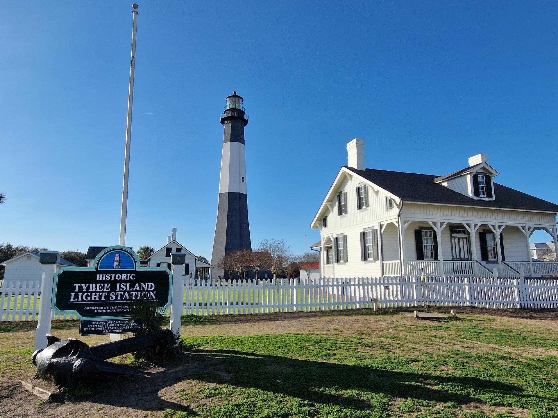 A tall black and white lighthouse next to a white house under a clear blue sky.