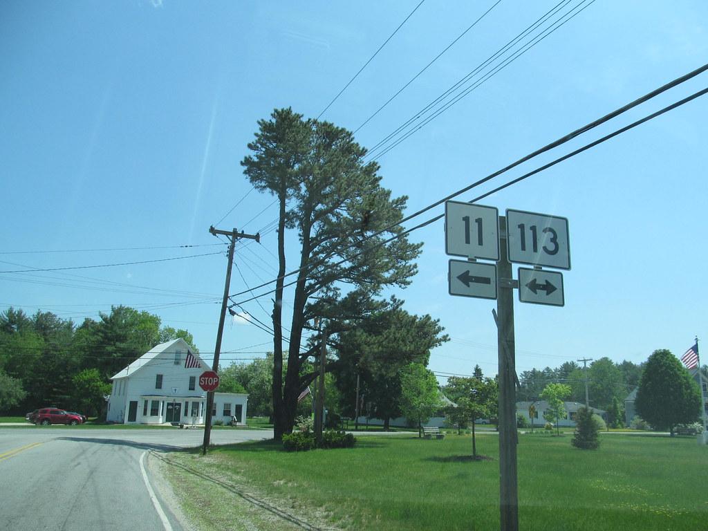 Road signs, power lines, and a white building under a bright blue sky.