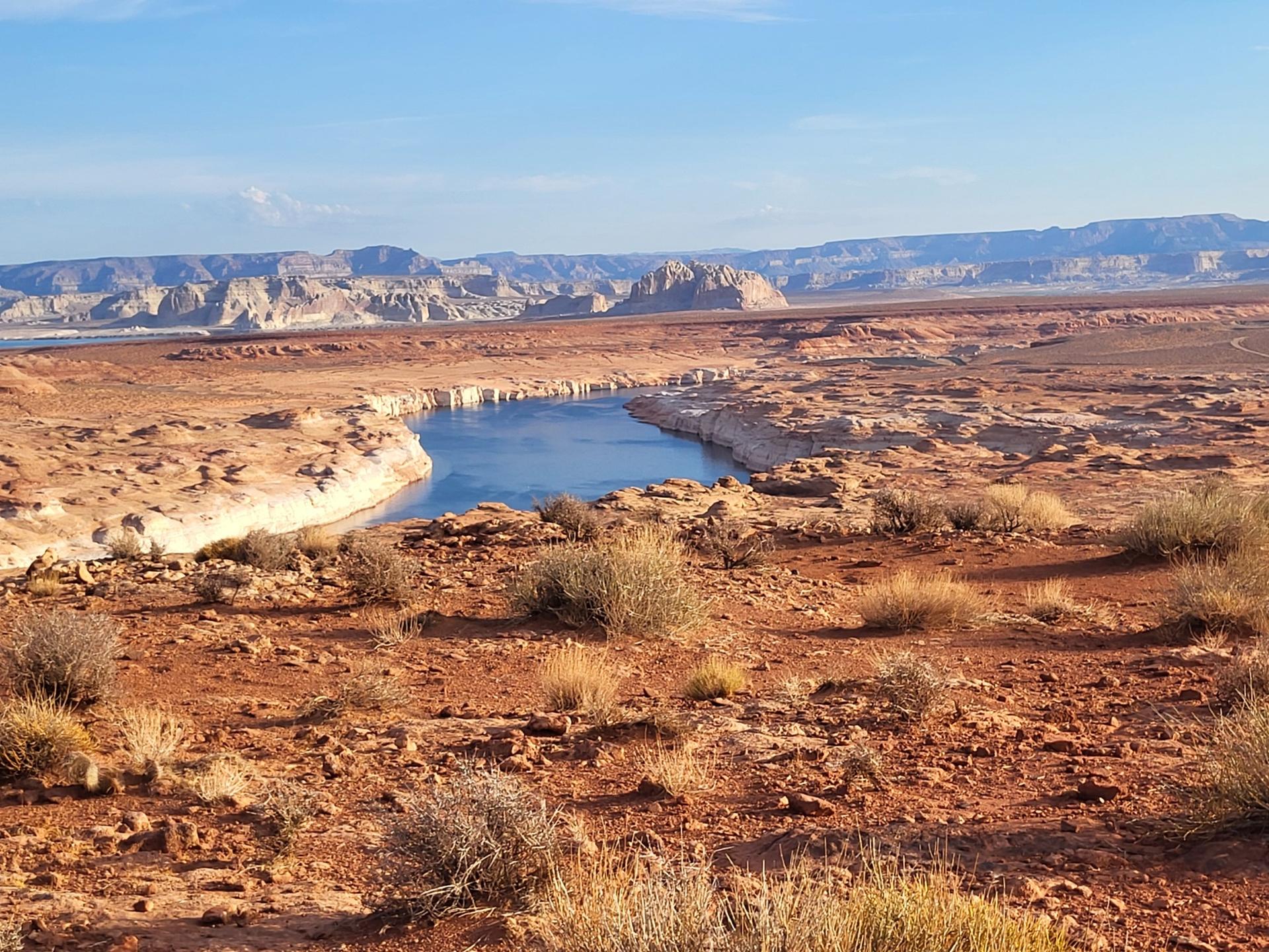A blue river flows through a red desert landscape with sparse brush.
