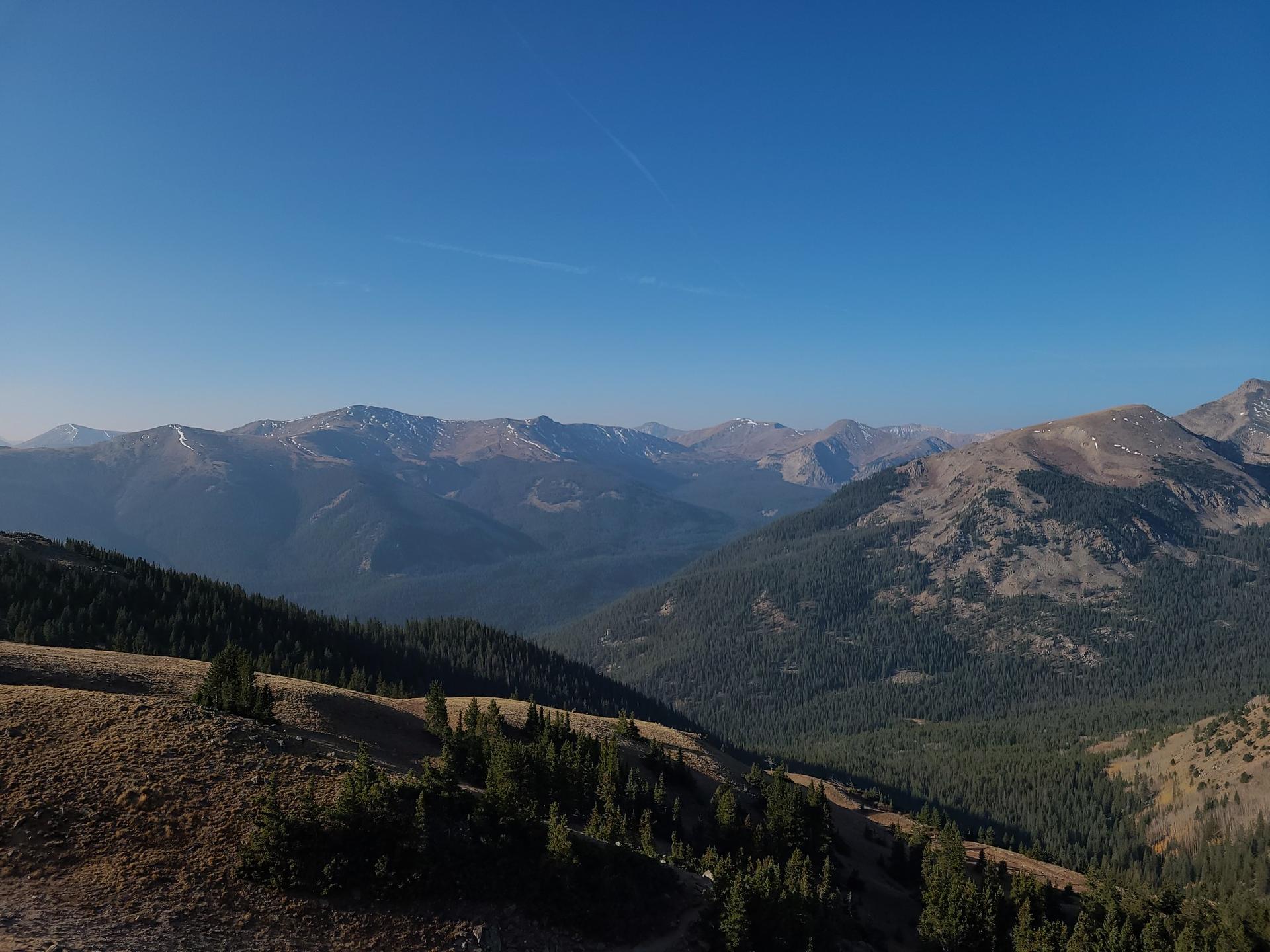 Expansive mountain landscape with forested valleys and clear blue sky.