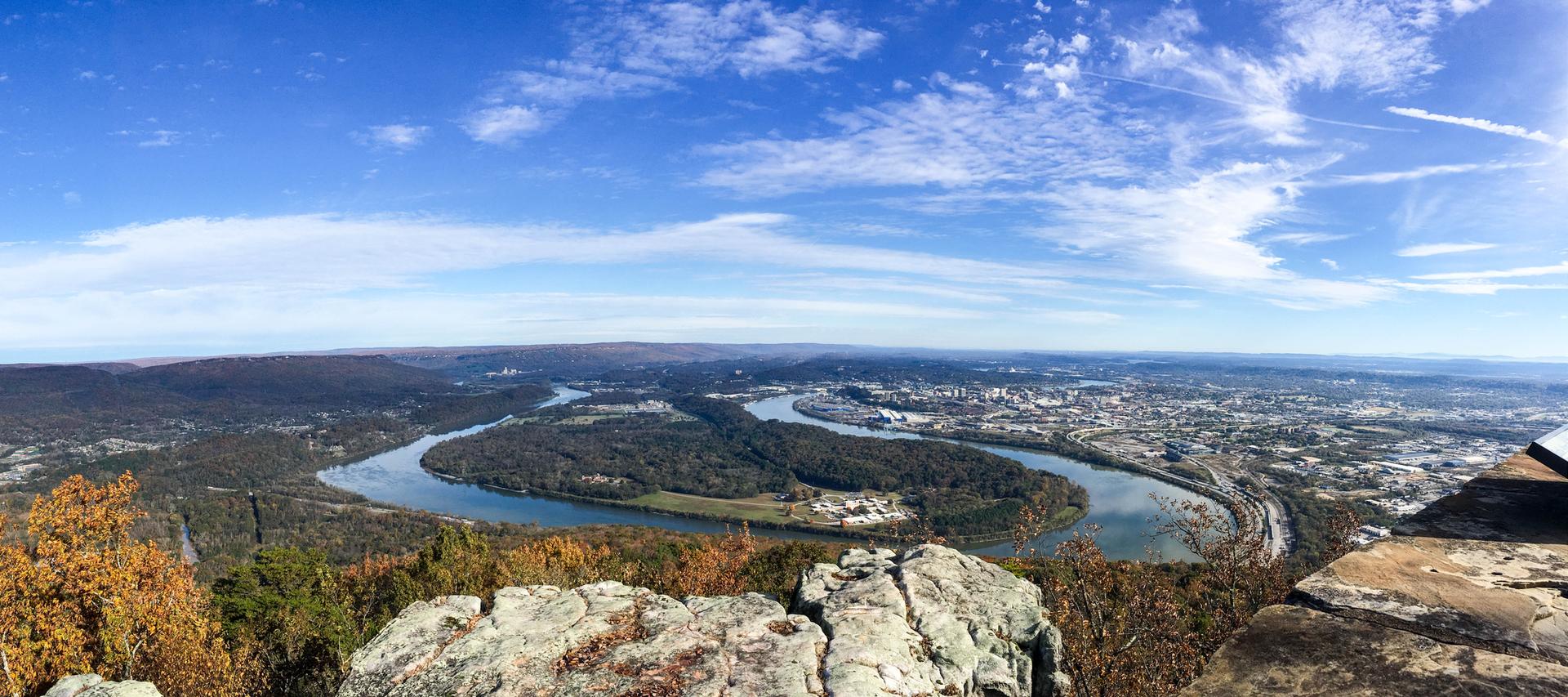 Panoramic view of a winding river and city under a bright blue sky.