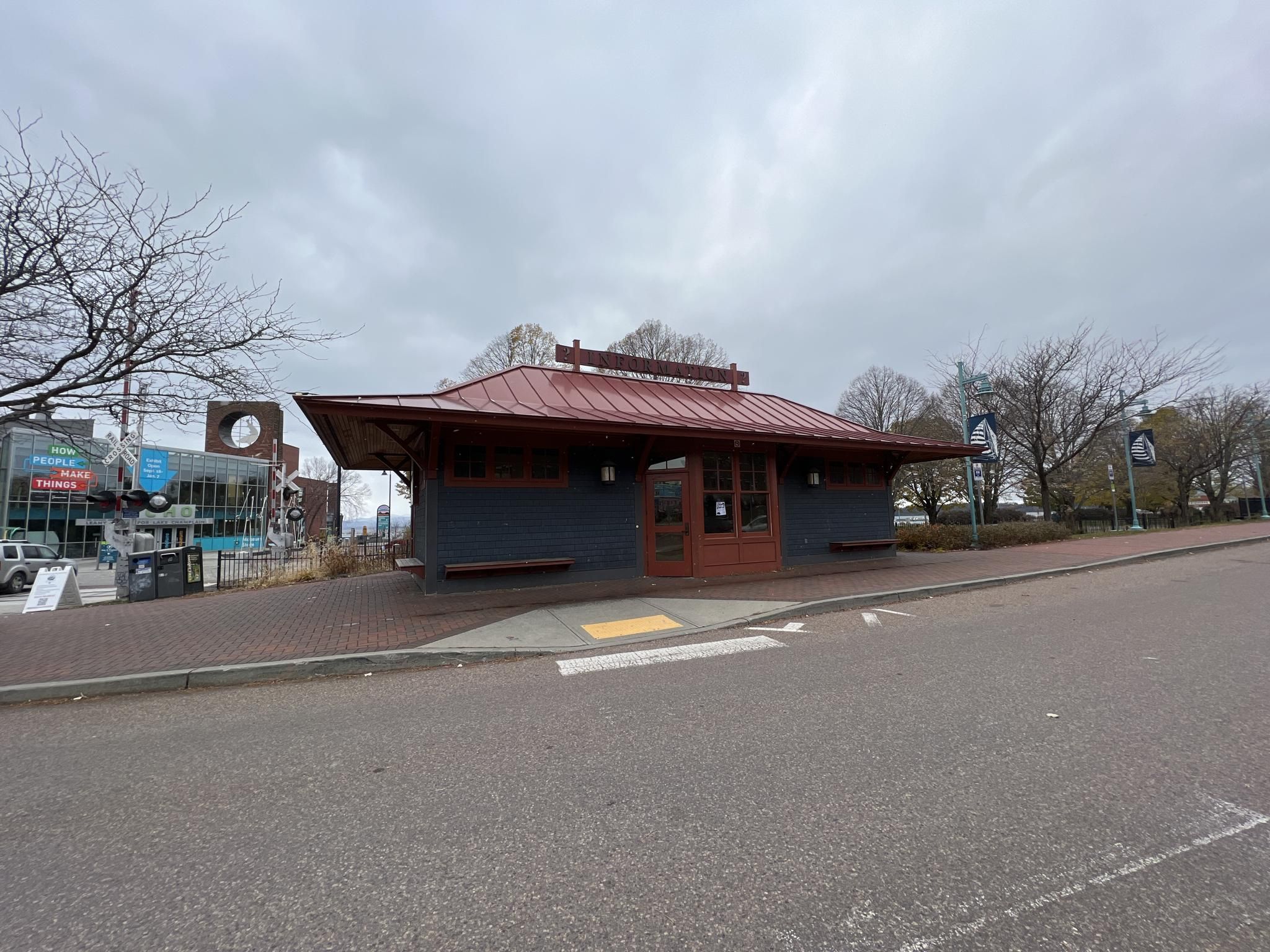 A small building with a red roof sits beside a paved street on a cloudy day. - Barge Canal loop from Burlington
