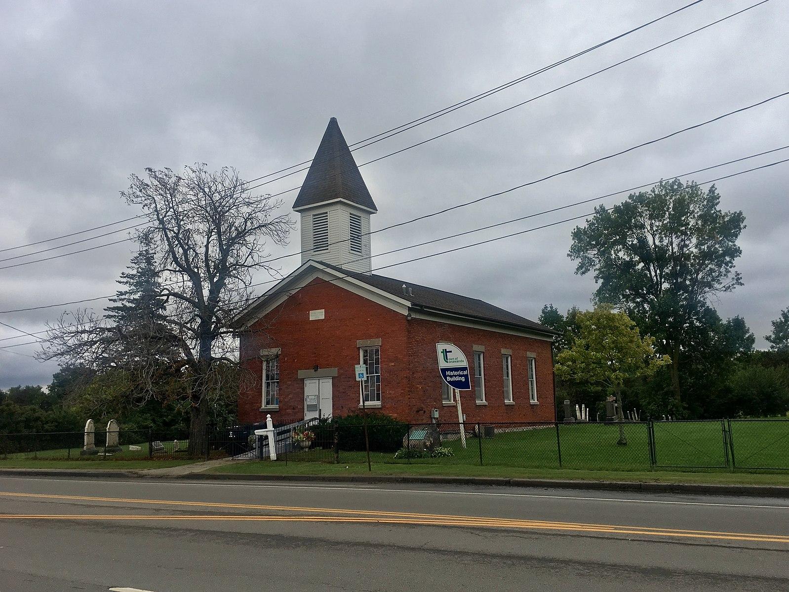 A red brick church with a white steeple next to a road on a cloudy day.