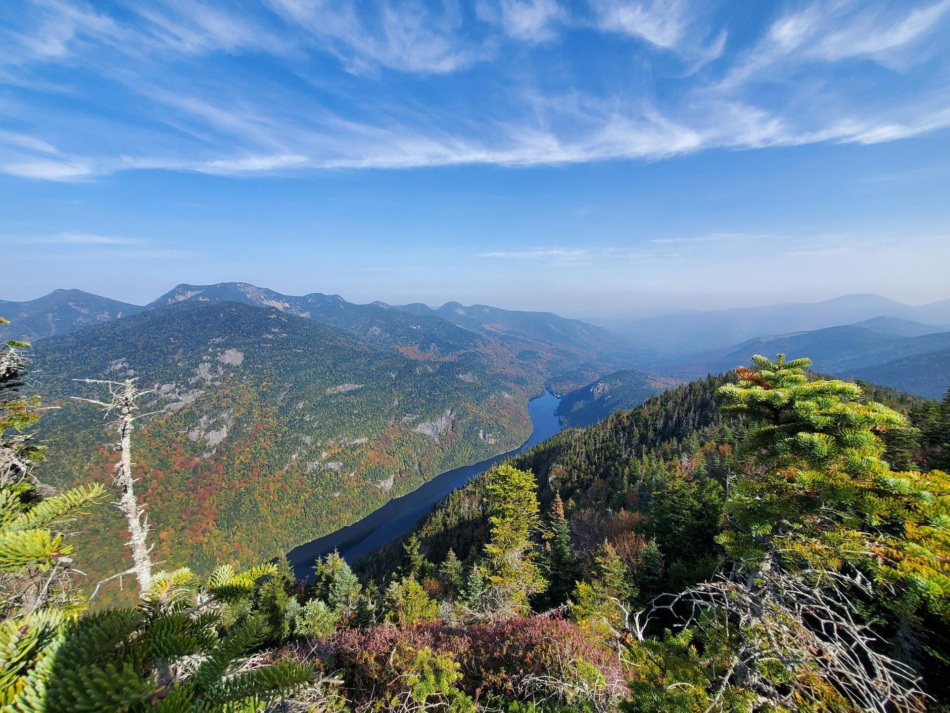 Panoramic view of mountains, a lake, and autumn foliage under a blue sky.