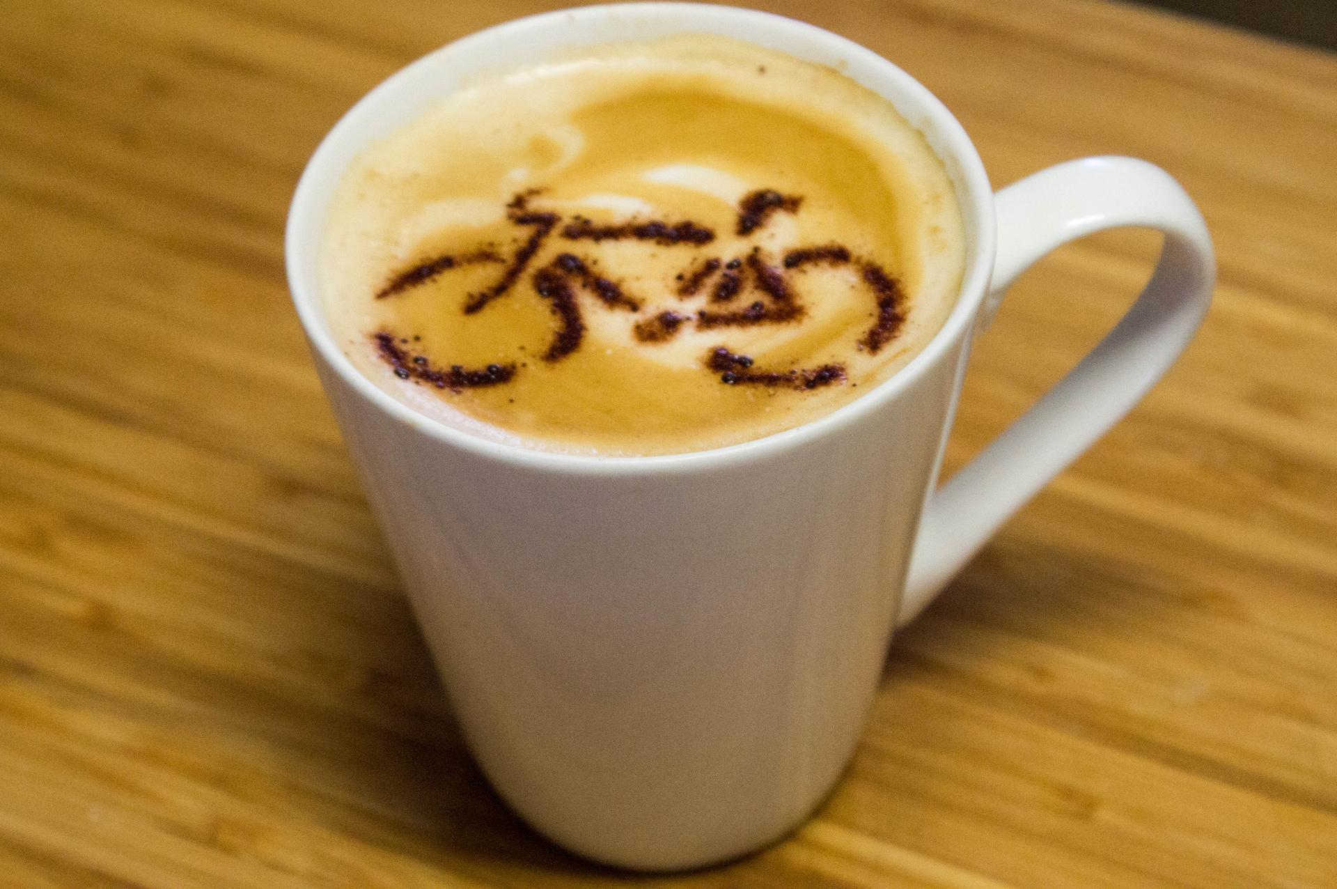 A white mug of coffee with a bicycle design in the foam on a wooden table.