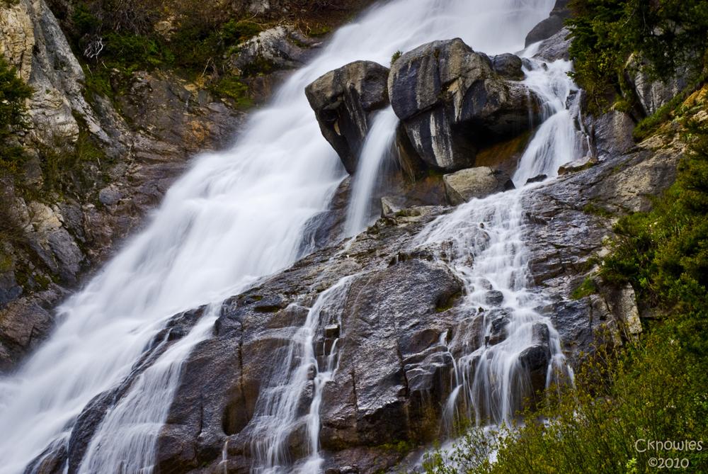 Powerful waterfall cascading over dark rocks with green foliage, long exposure.