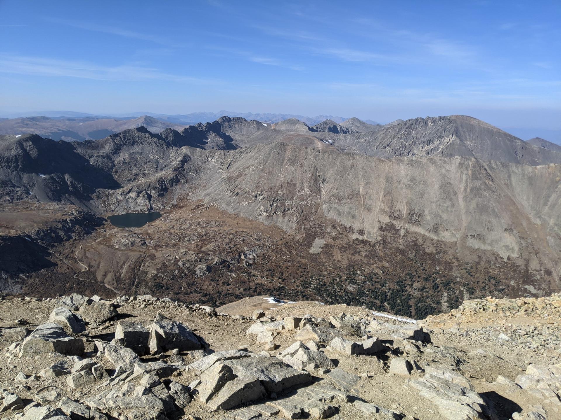Panoramic view of rugged mountains and a lake from a rocky peak.