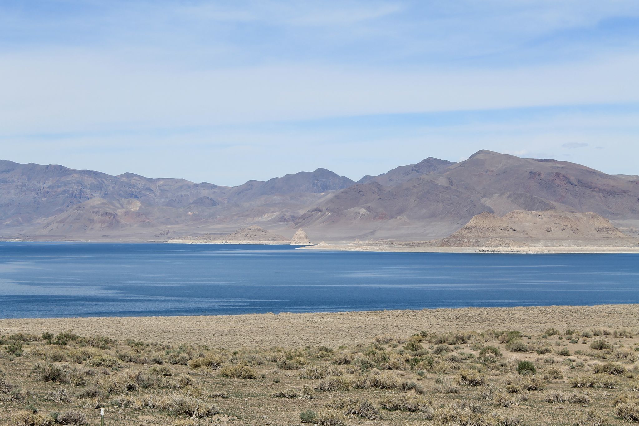 Blue lake surrounded by dry, brushy land and distant, rocky mountains under a bright sky. - Spanish Springs to Pyramid Lake via Pyramid Highway