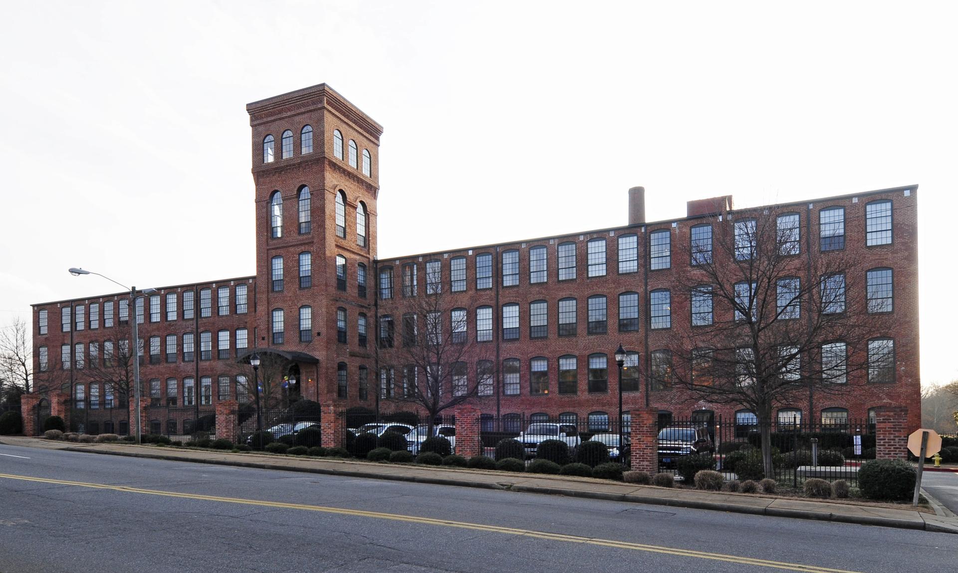 Large brick industrial building with a tall tower under a bright sky.