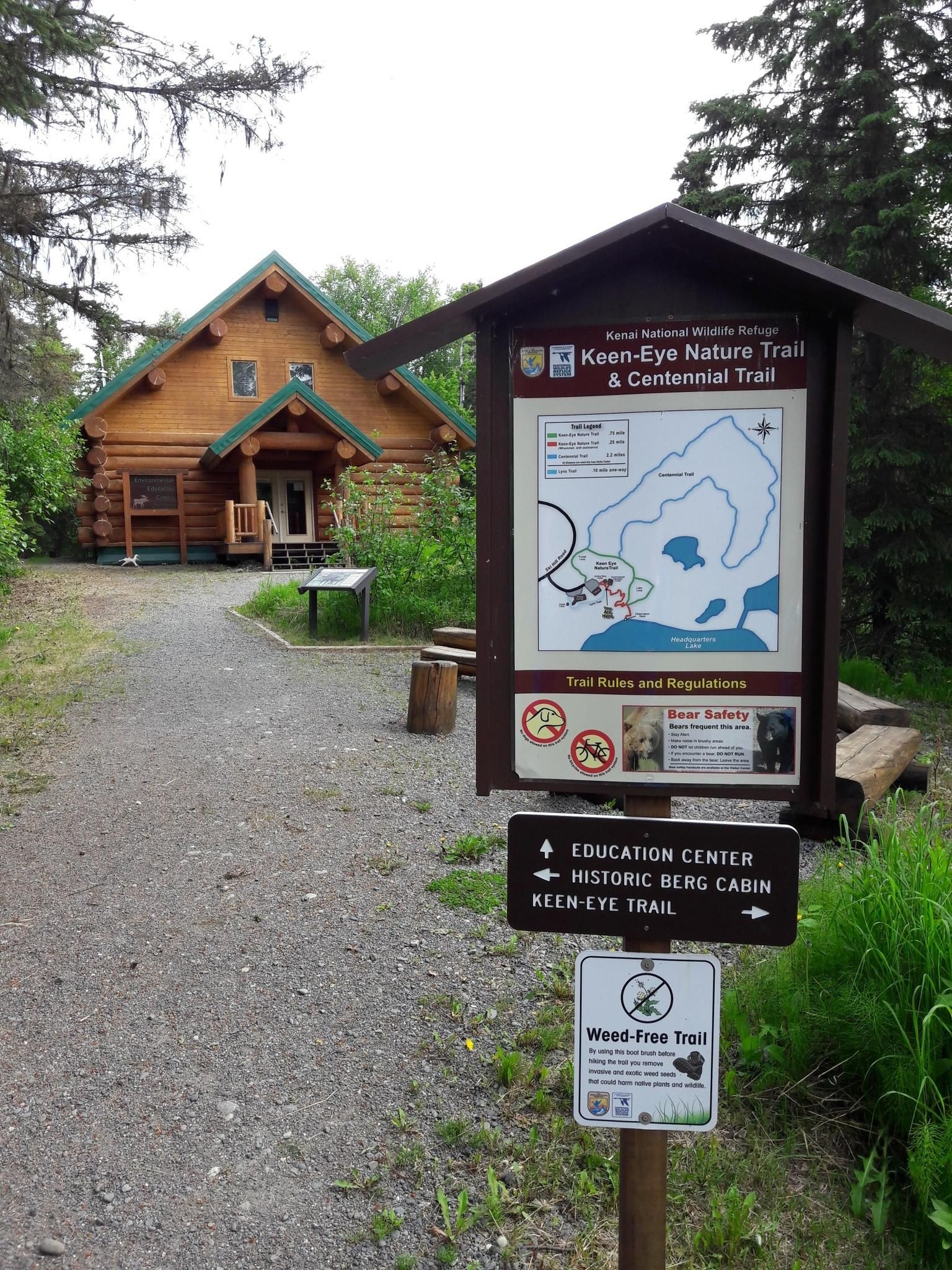 Trailhead sign and log cabin in a wooded area on an overcast day. - Kenai National Wildlife Refuge