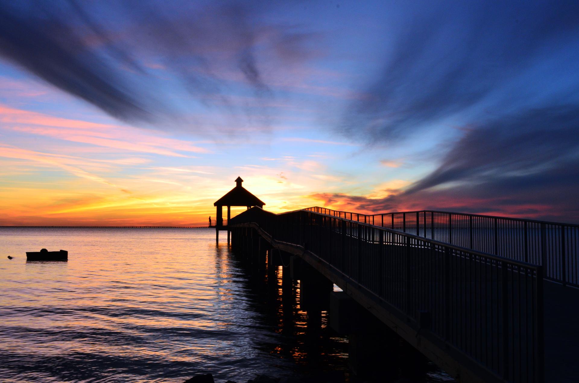 Dramatic sunset over water with a silhouetted pier and gazebo.