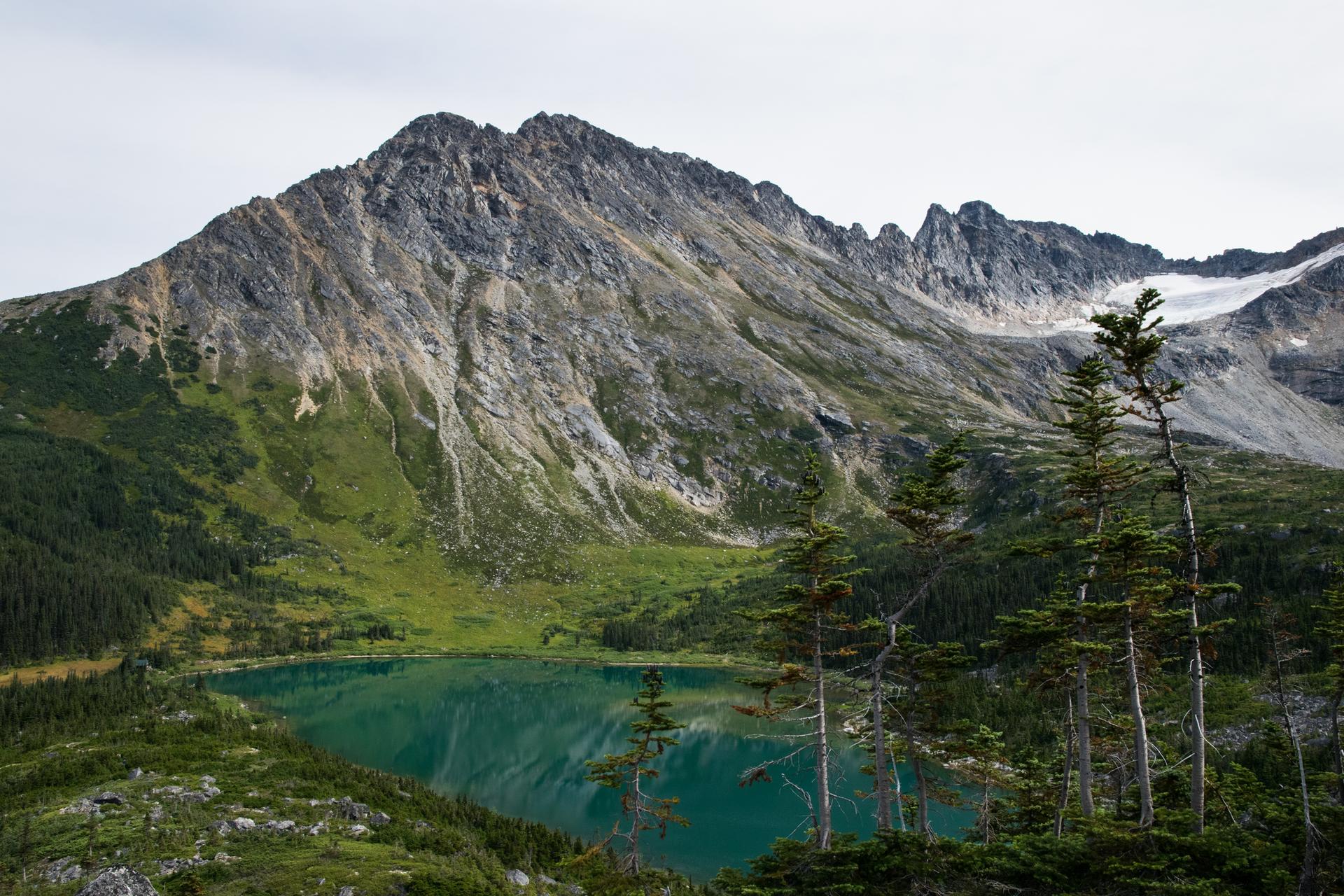 Turquoise alpine lake below a rugged mountain peak and glacier, cloudy day.