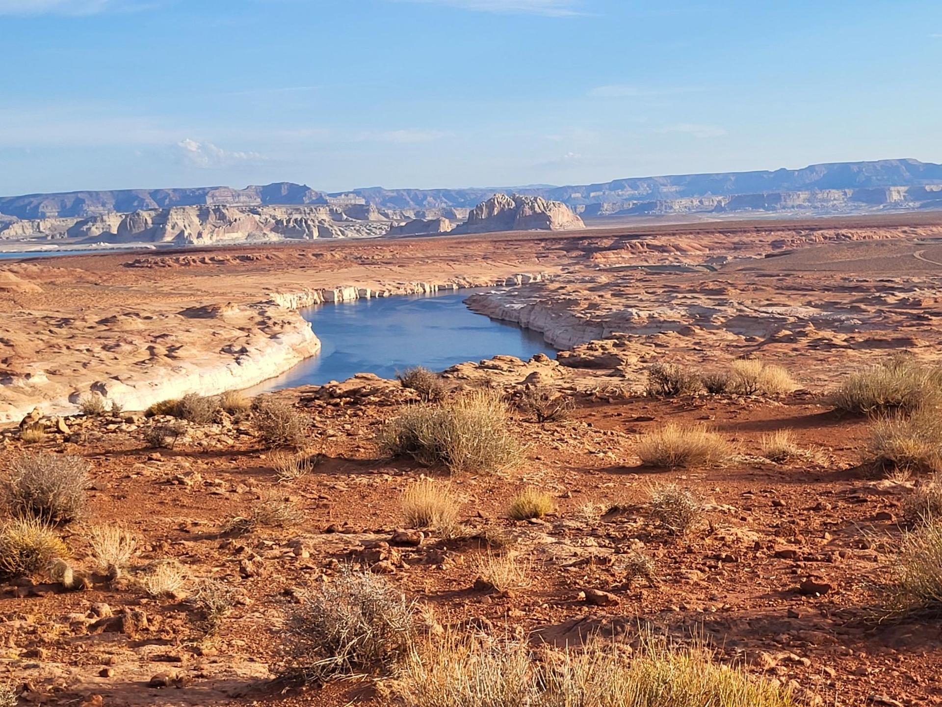 Blue lake winding through a vast red rock desert under a bright sky.
