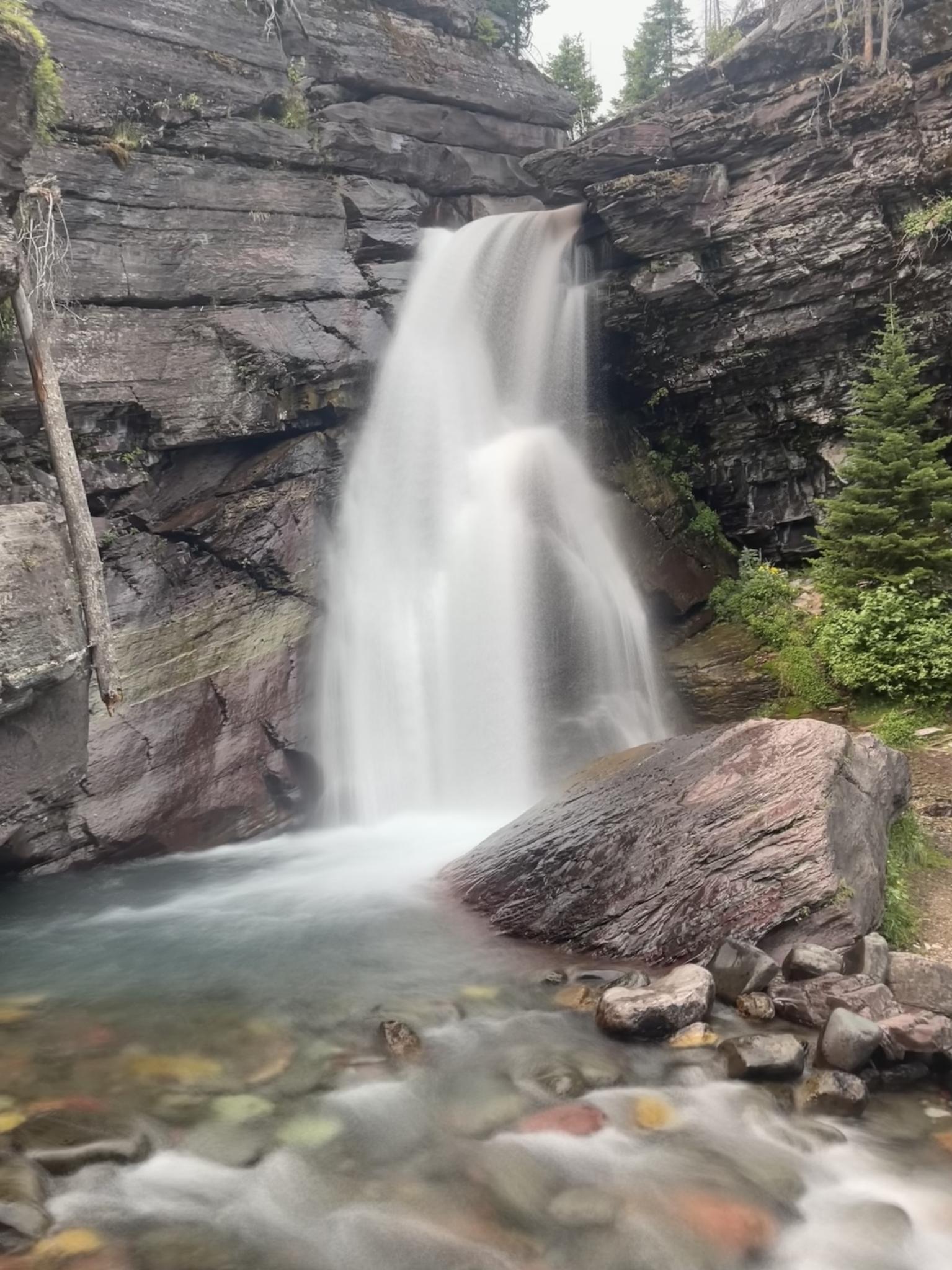 A powerful waterfall cascades over dark rock formations into a clear stream.