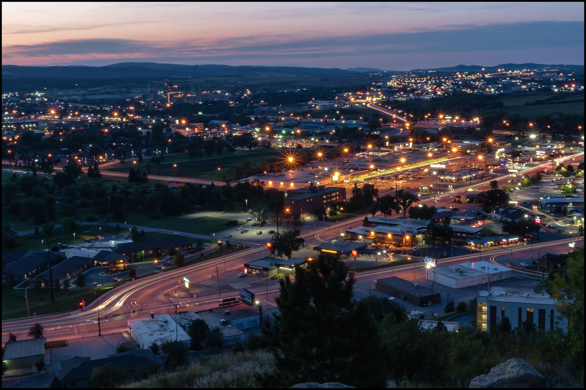 Vibrant city lights illuminate an urban landscape at twilight from above.