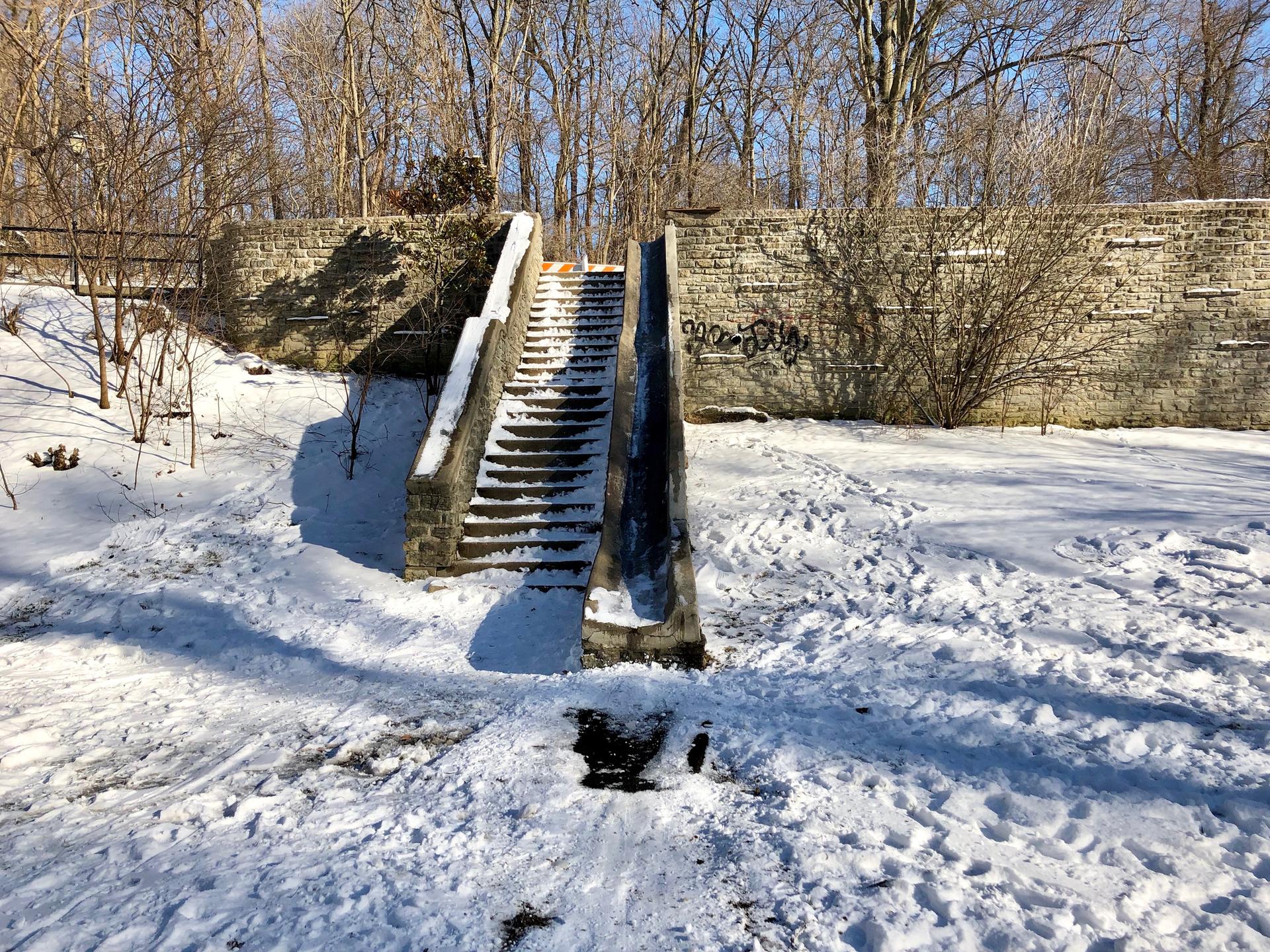 Snow-covered stone stairs and slide next to a wall on a sunny winter day.