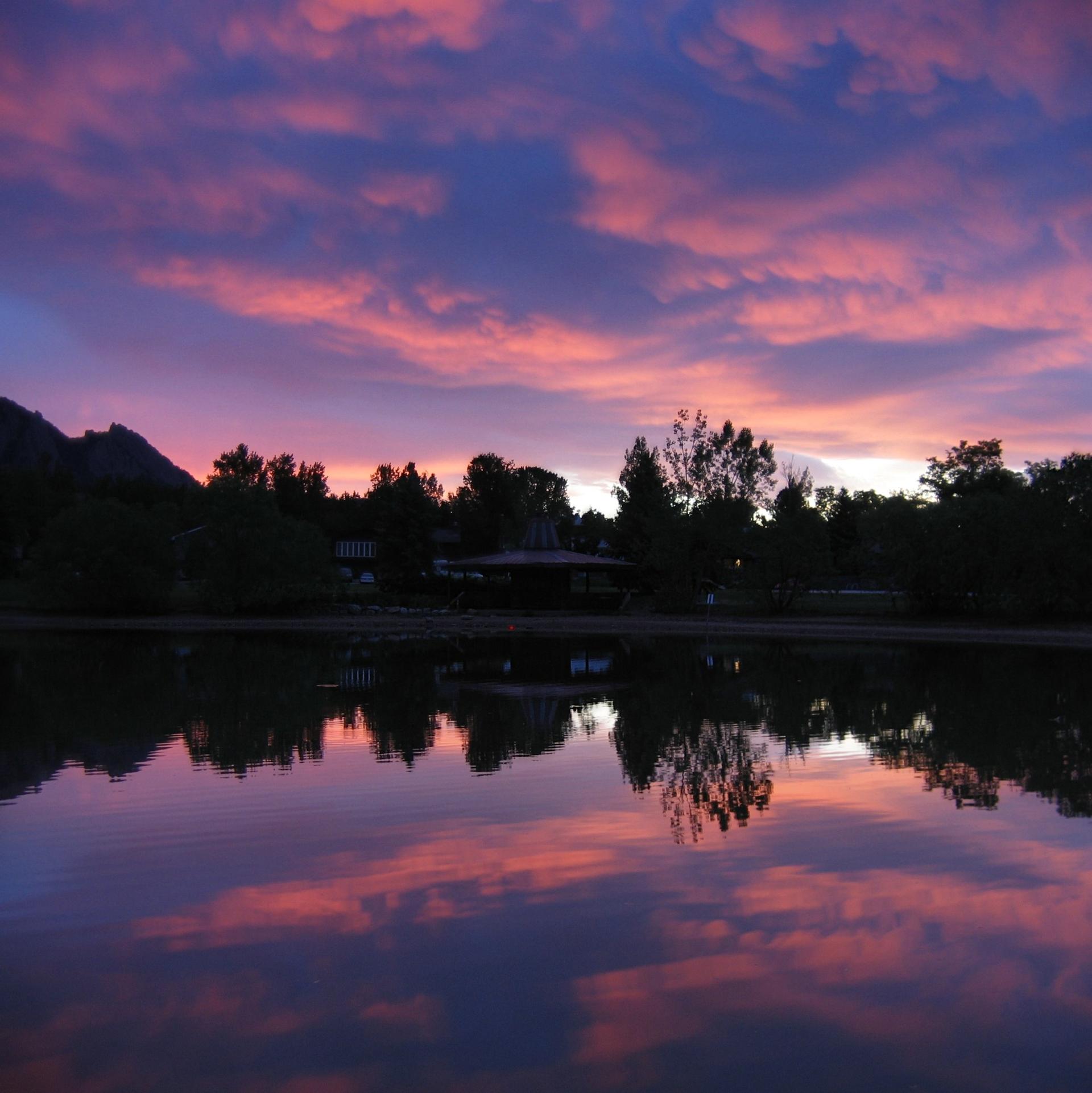 A serene lake reflects a dramatic pink and purple sunset over silhouetted trees.