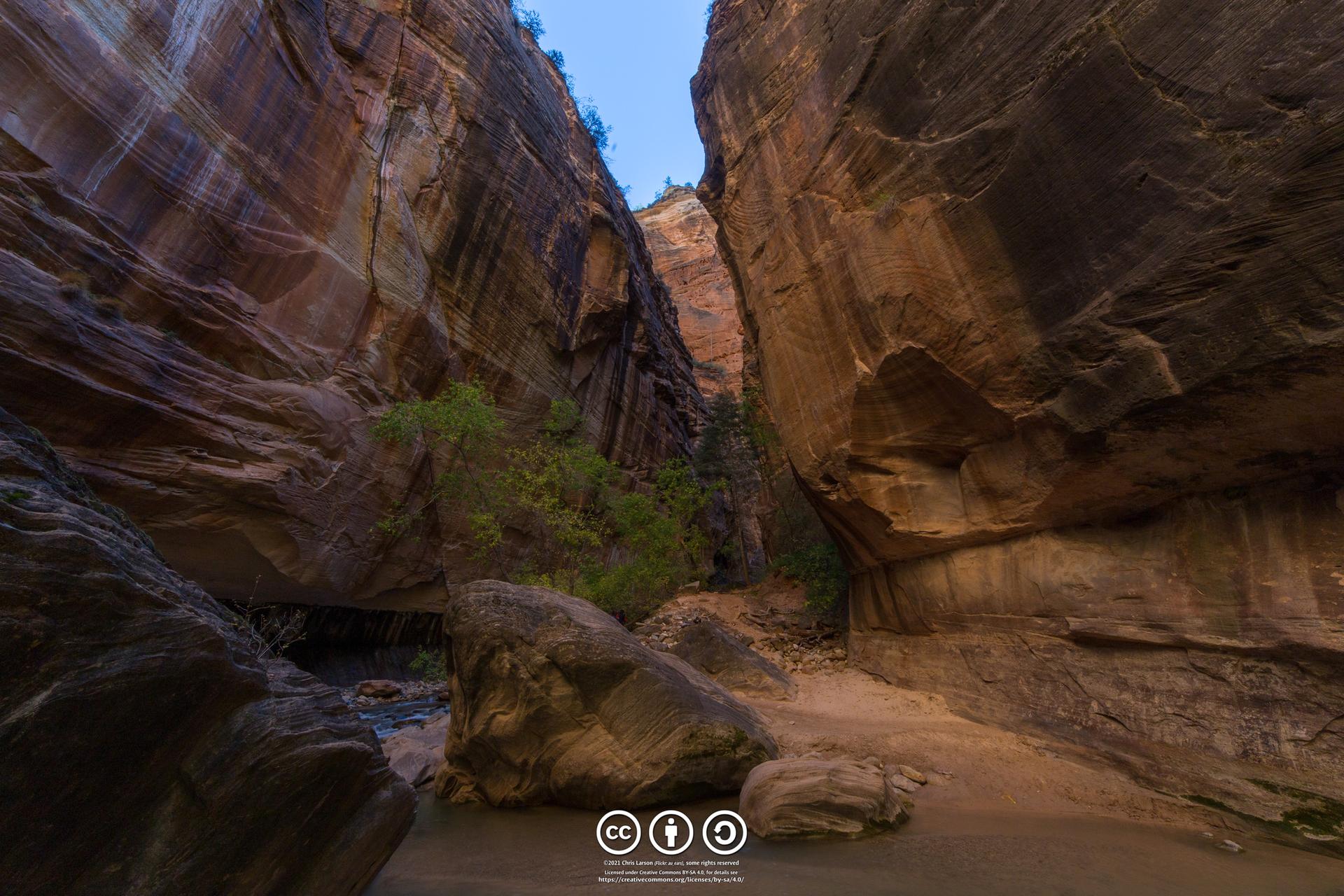 Towering, dark rock walls of a narrow canyon with a glimpse of sky.