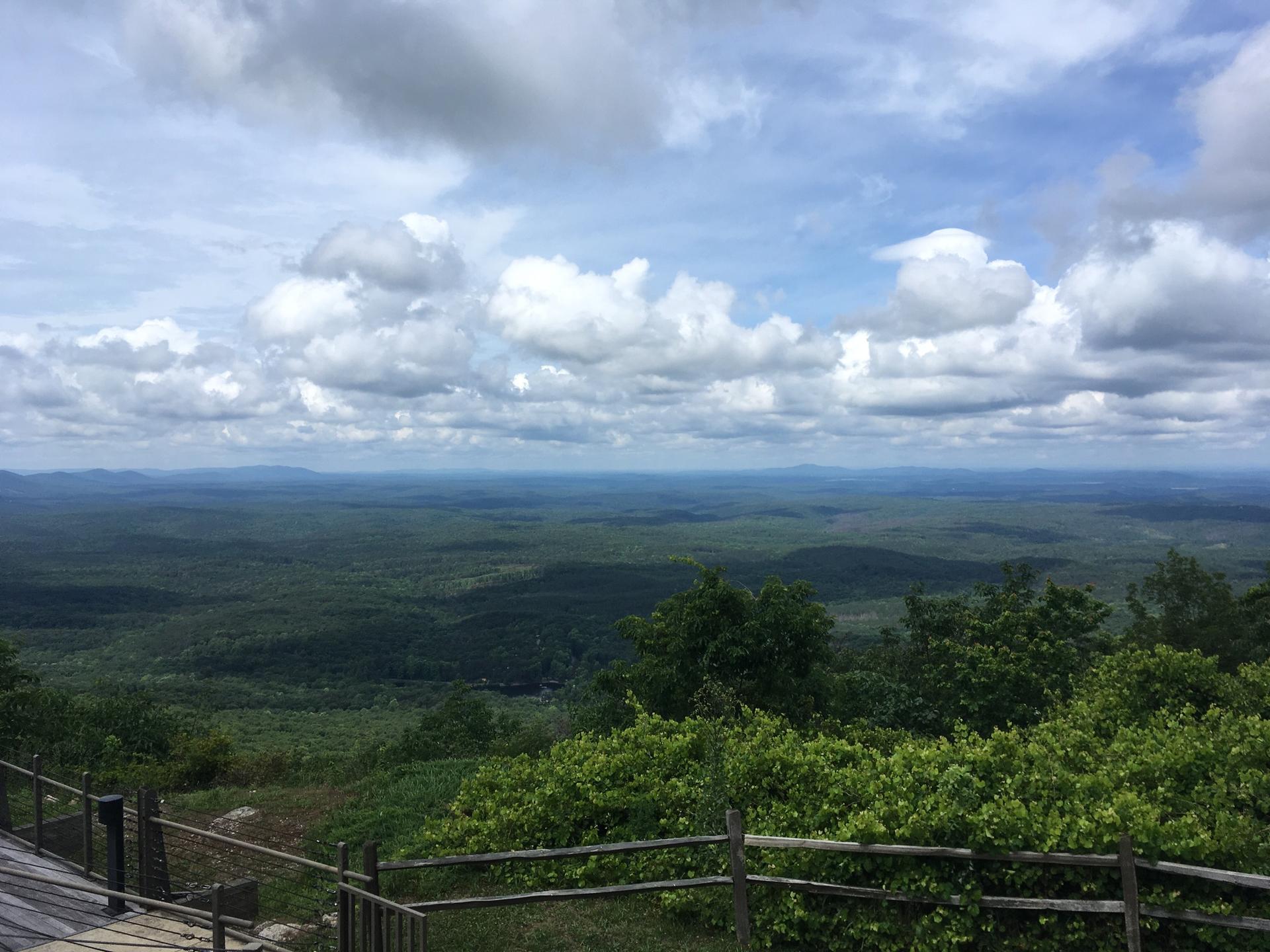 Expansive view of green forested hills under a bright, cloudy sky.