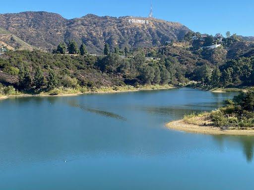 Calm blue water reflecting a distant sign on a sunny, hilly landscape.
