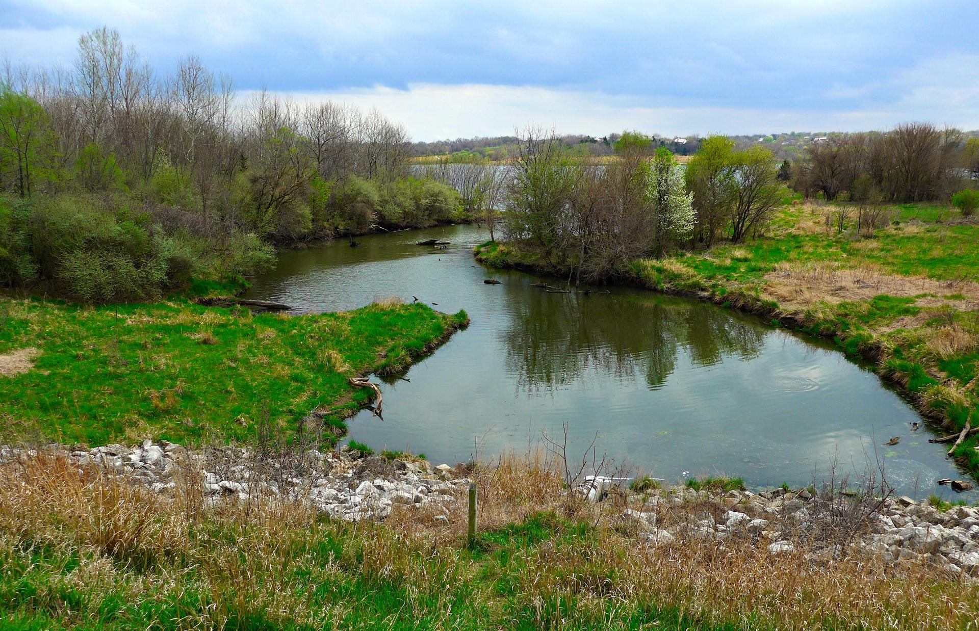 Winding river with green banks and trees under a cloudy sky.