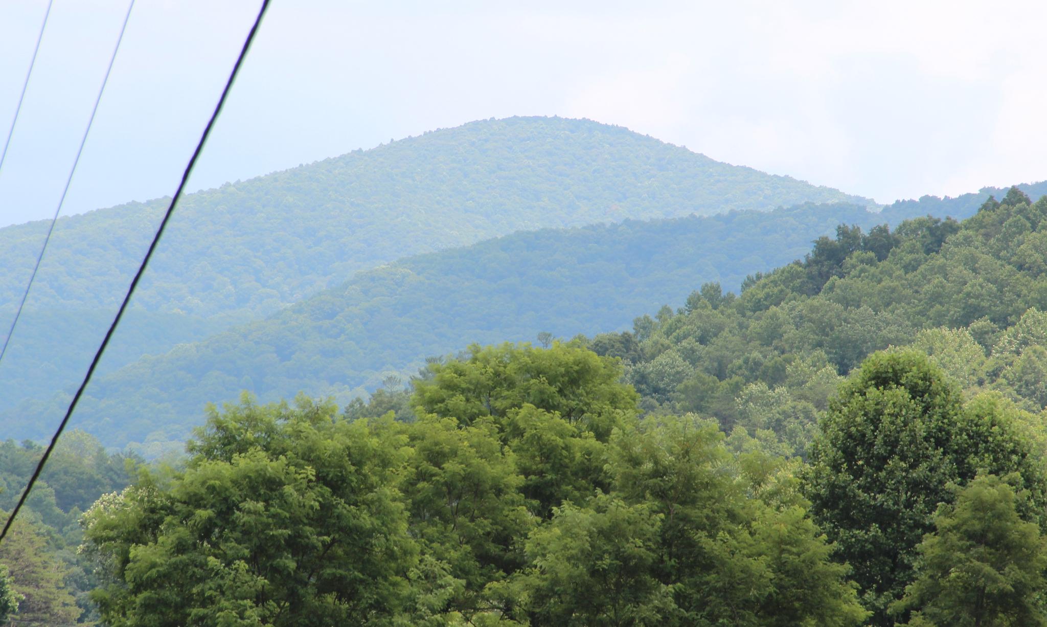 Distant green mountains under a hazy sky, with power lines in the foreground.