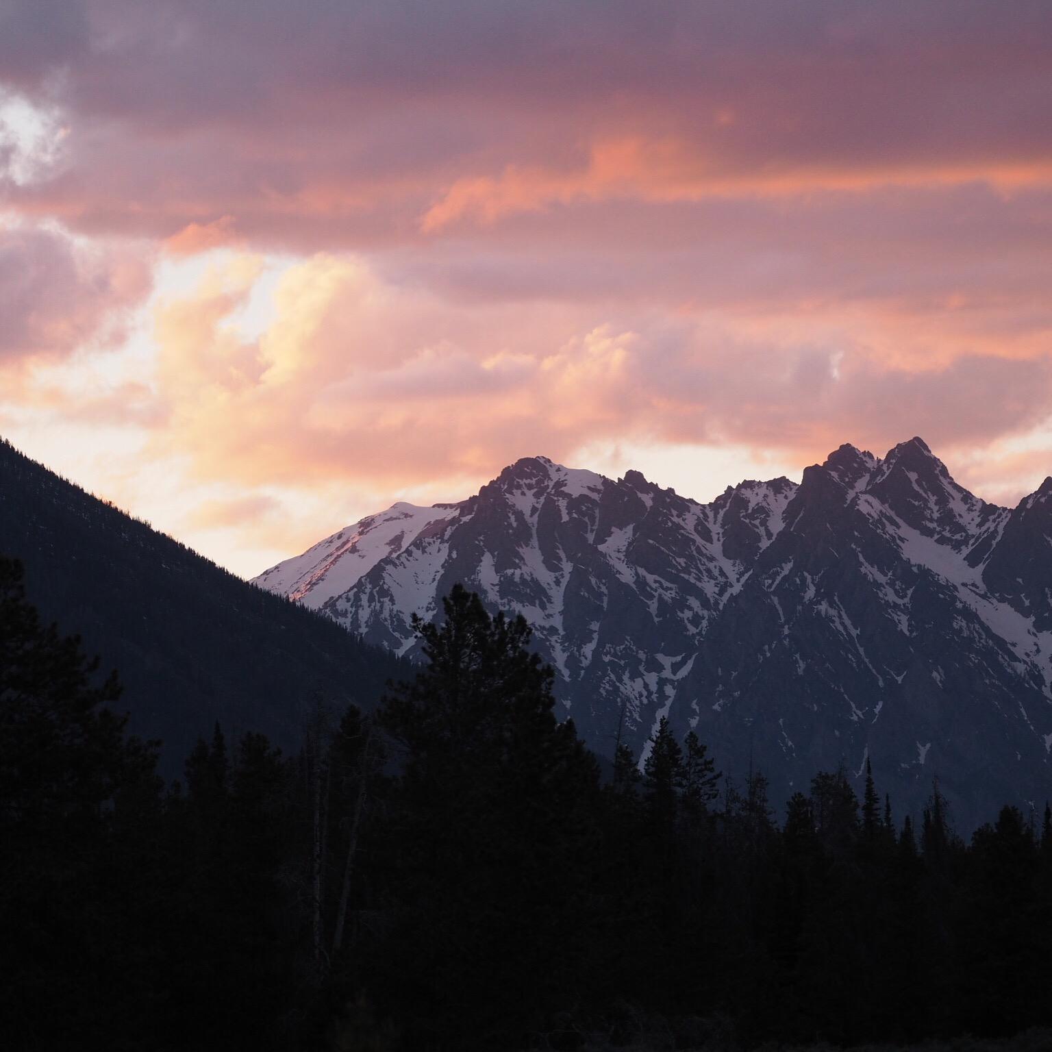 Snow-capped mountains and dark forests under a vibrant sunset sky.