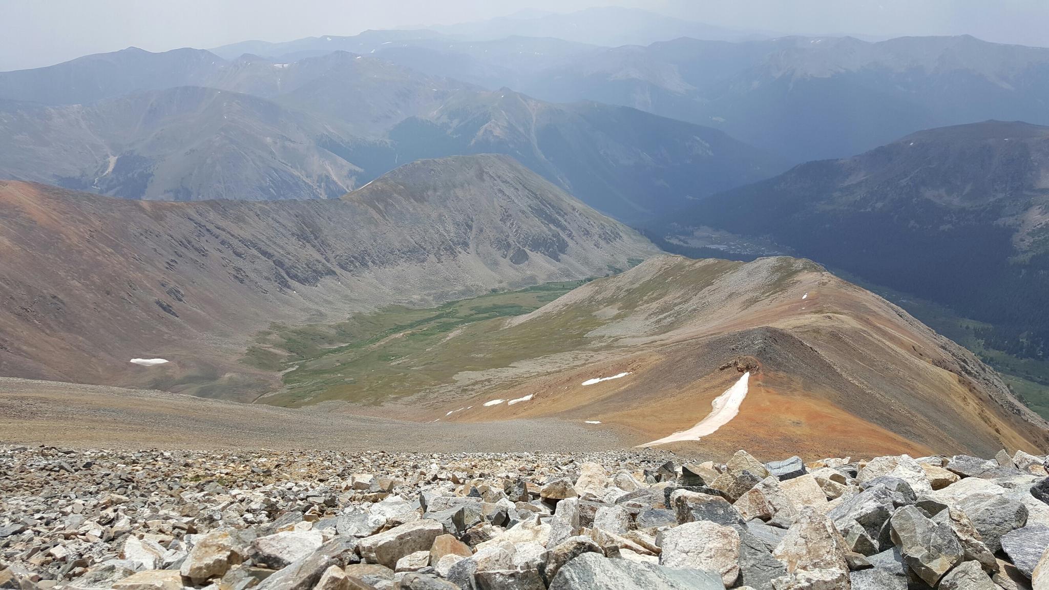 A rocky mountain slope in the foreground overlooks hazy distant peaks and a valley.
