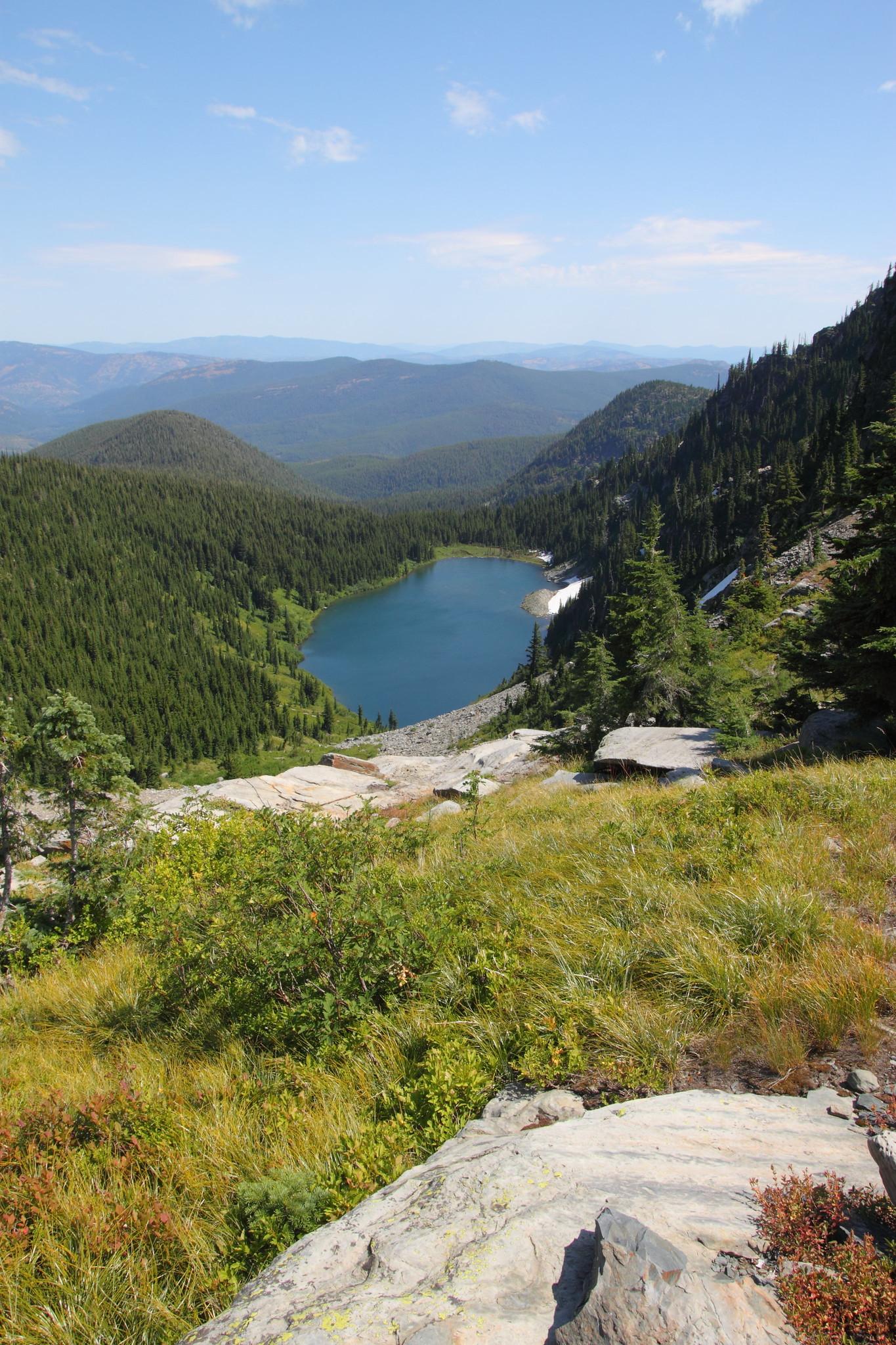 Blue mountain lake nestled in a valley, surrounded by green forested hills.