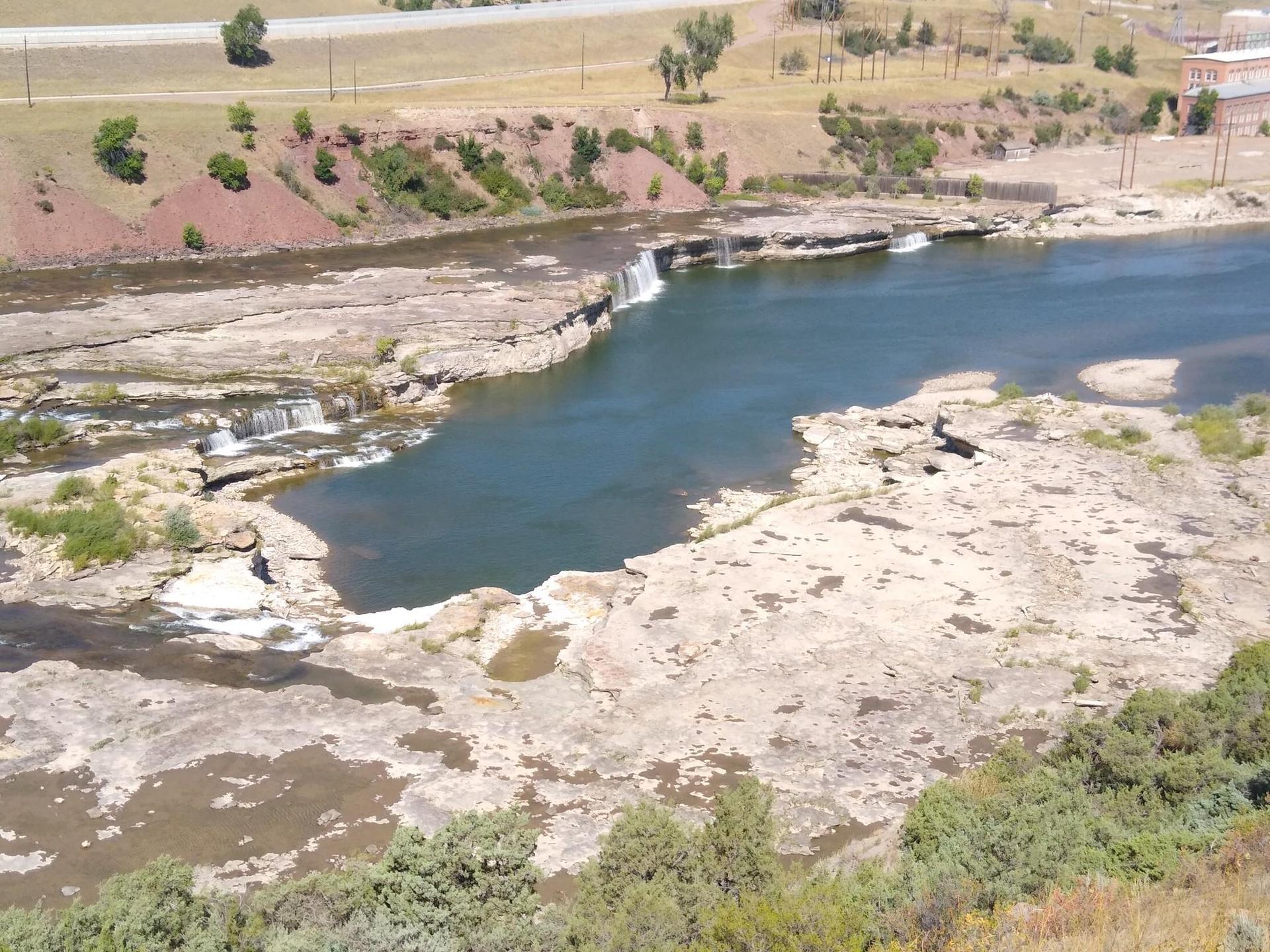 Sunny aerial view of a wide river with rocky banks and small waterfalls.