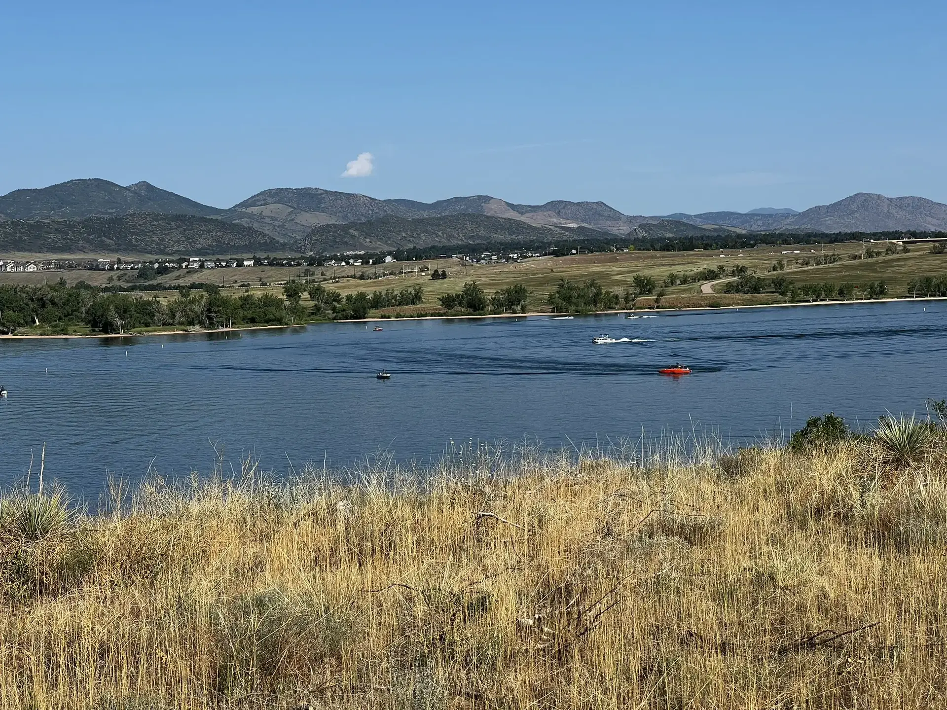 Boats on a large lake with distant mountains under a clear sky.