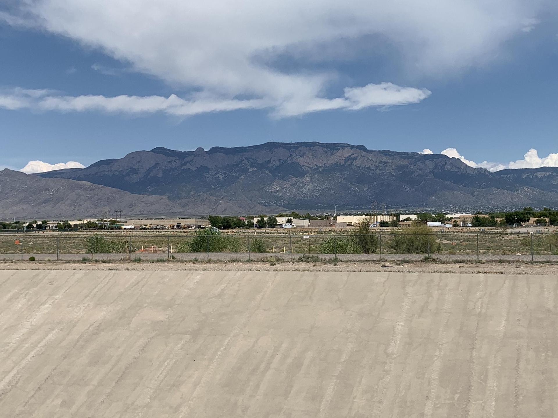 Distant mountains overlook an arid landscape with buildings under a cloudy sky.