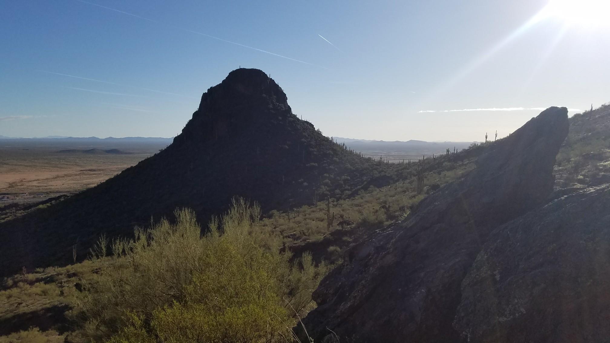 Dark mountain peak and ridge silhouetted against a bright, sunny sky.