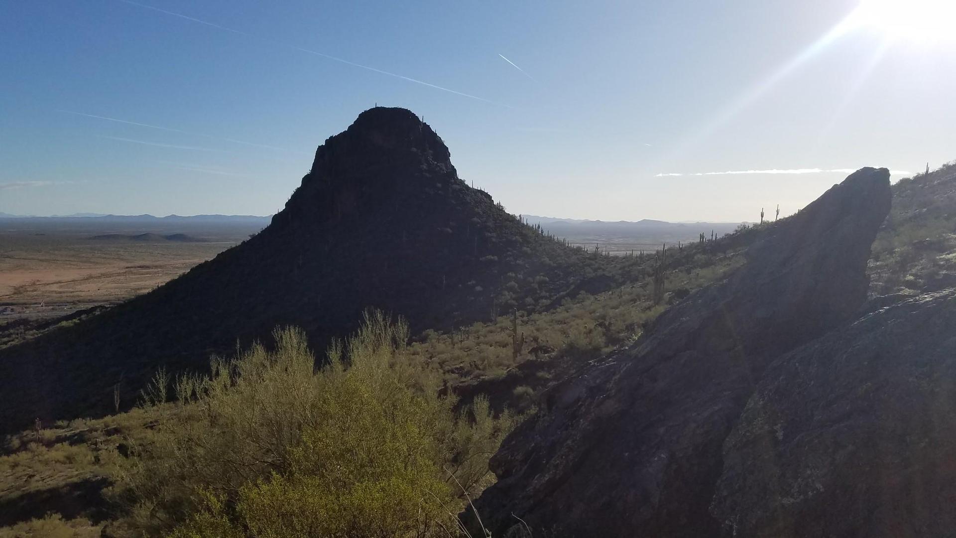 Dark mountain peak and ridge silhouetted against a bright, sunny sky.