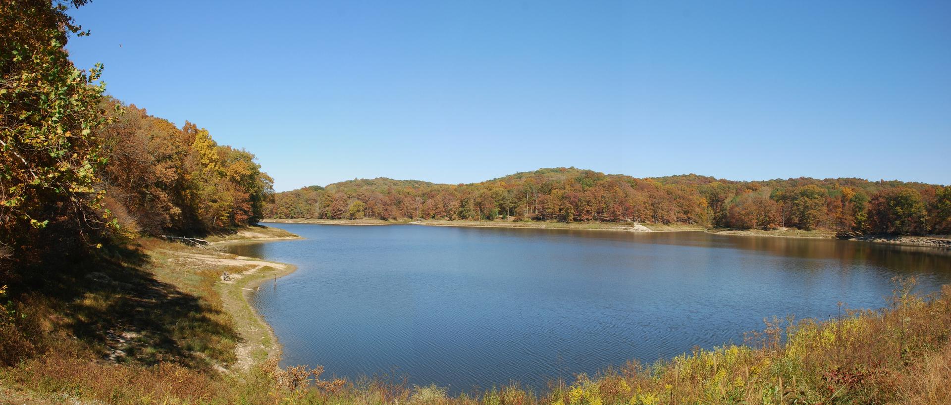 Vast lake bordered by colorful autumn trees and hills on a sunny day.