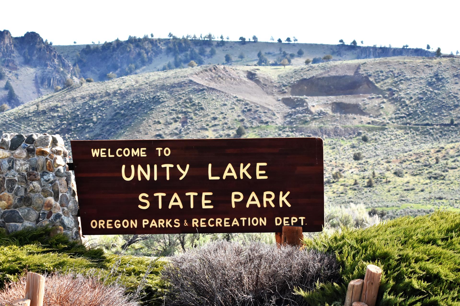 A wooden sign with a stone base in front of dry, rolling hills.