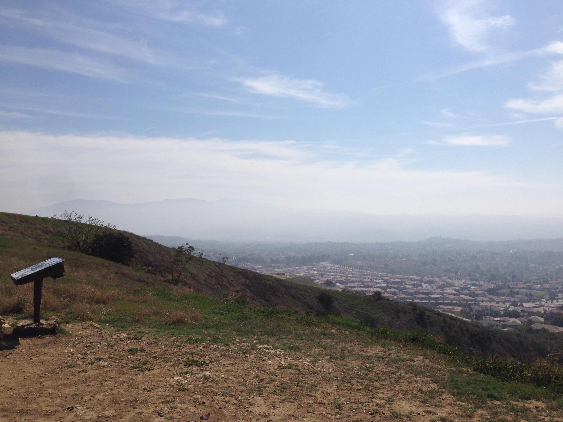 Grassy hillside overlooking a hazy valley with a distant town.