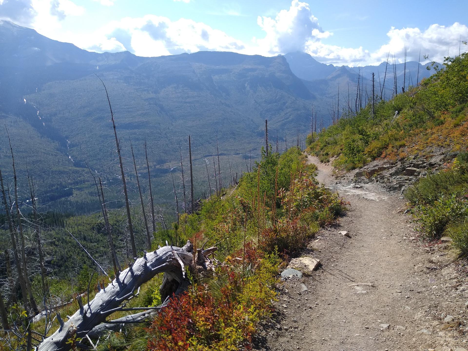 A narrow dirt trail traverses a steep mountain slope with valley views.