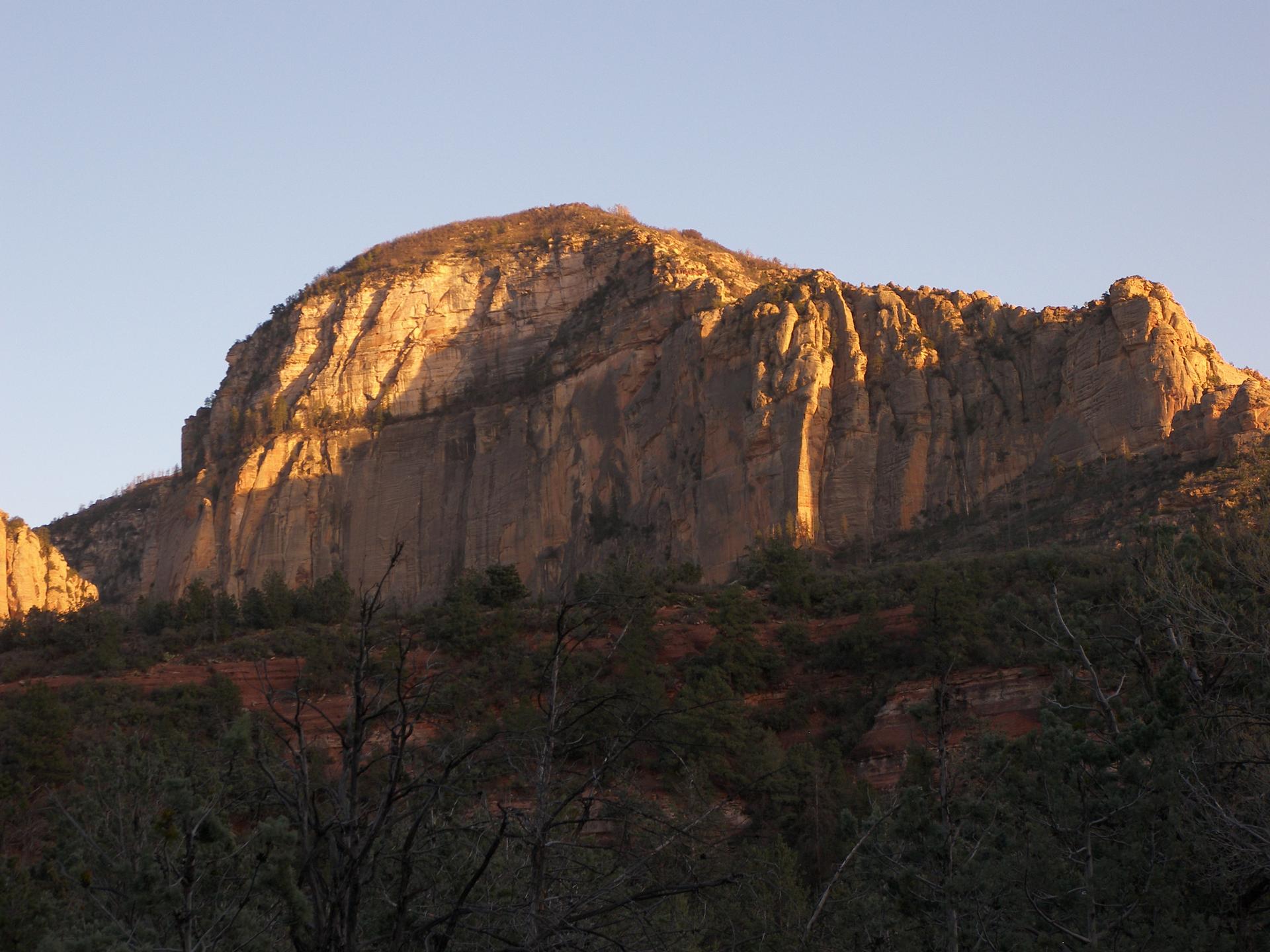 Golden light illuminates a rugged rock mountain with dark trees in the foreground.