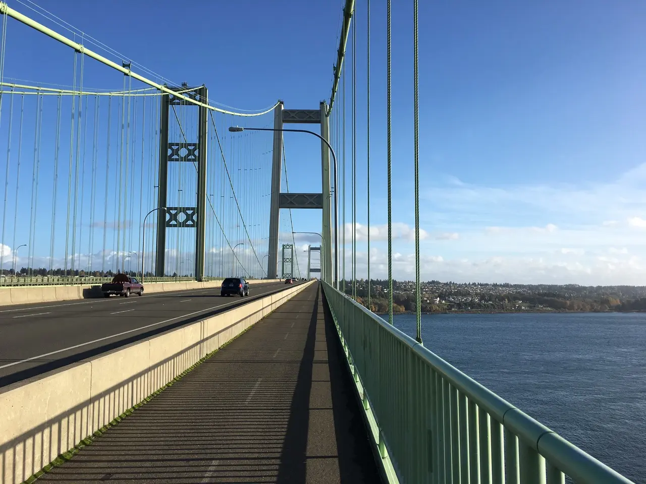 Cars on a suspension bridge over water under a clear blue sky.